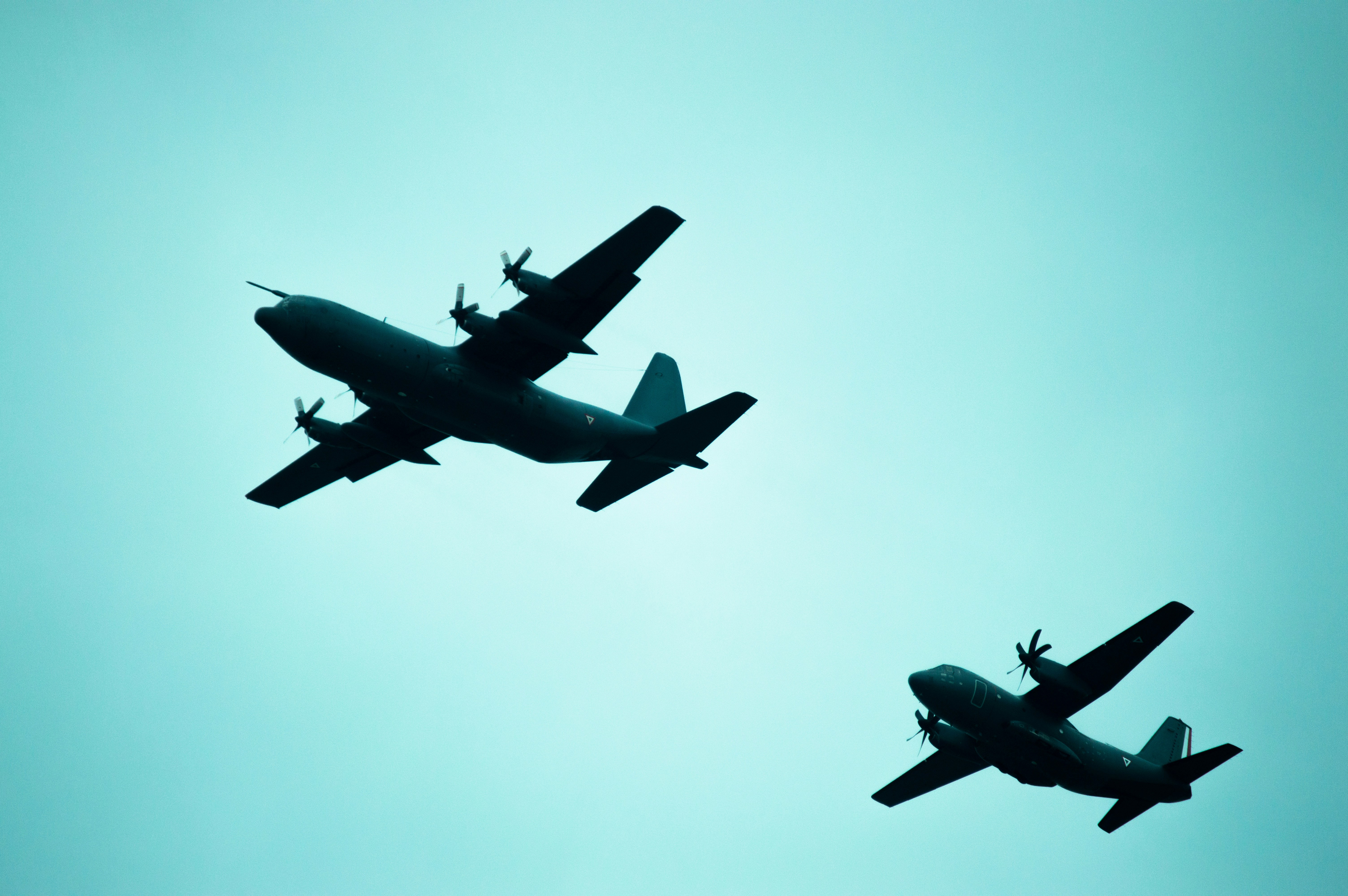 Two military planes fly across a blue sky.