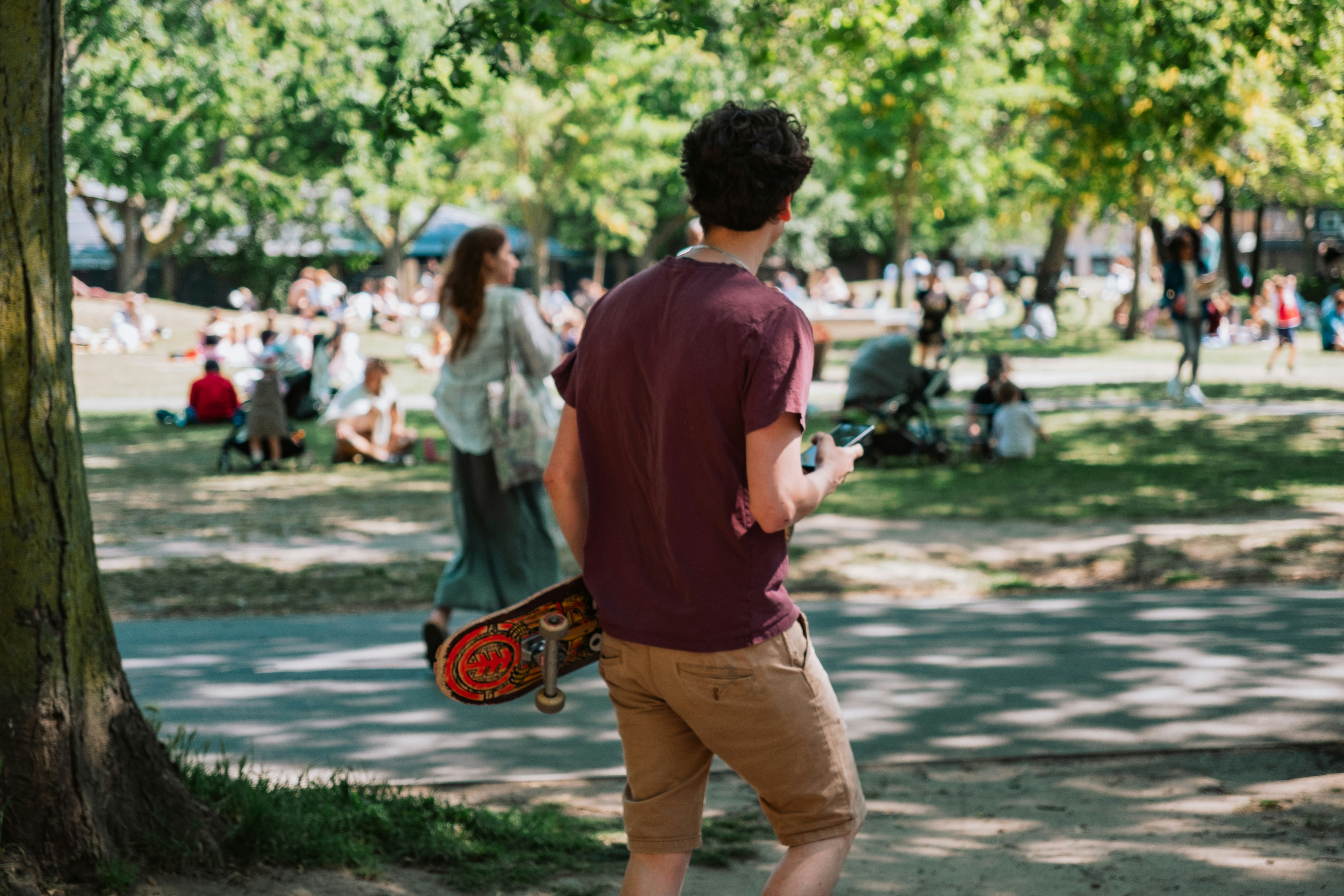 Teenager with skateboard walks in sunny park.