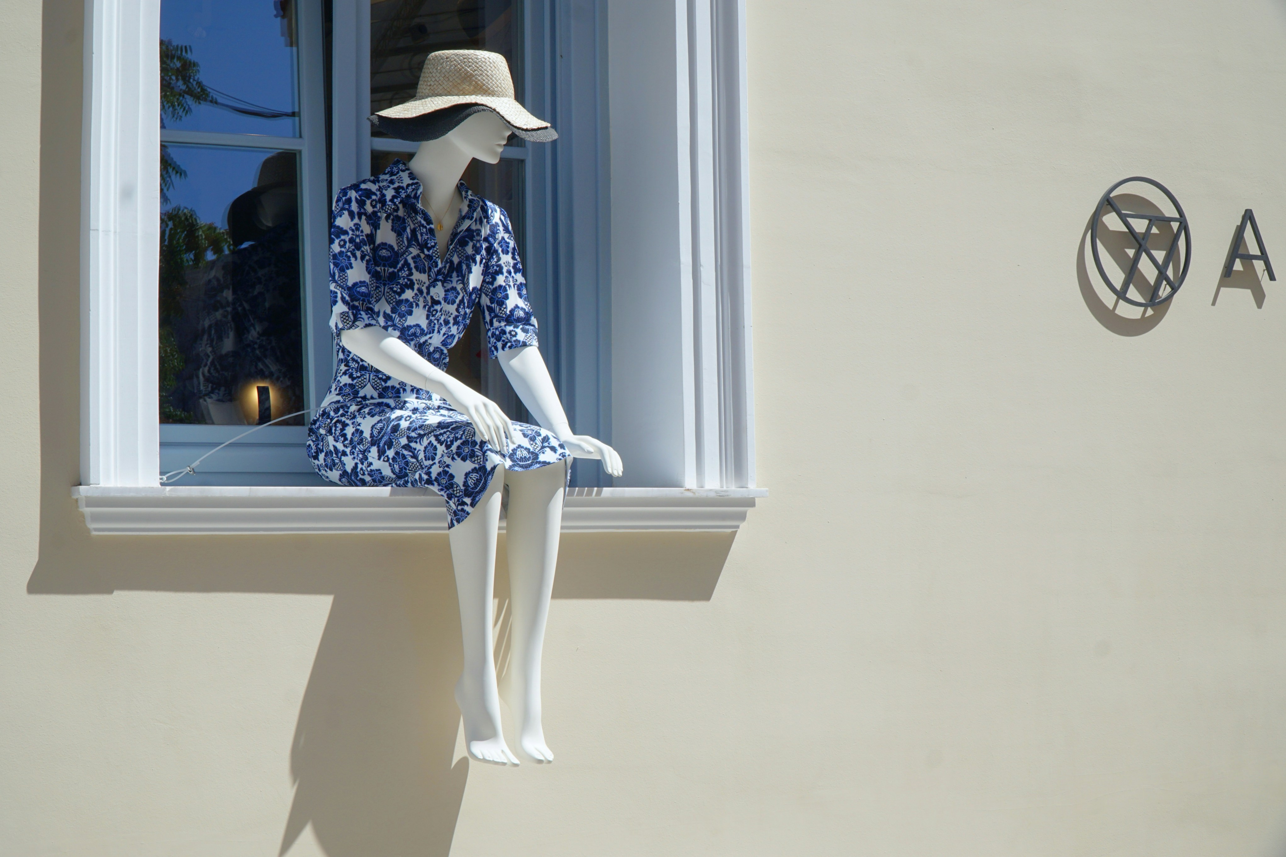 Mannequin sits in window, wearing a hat.