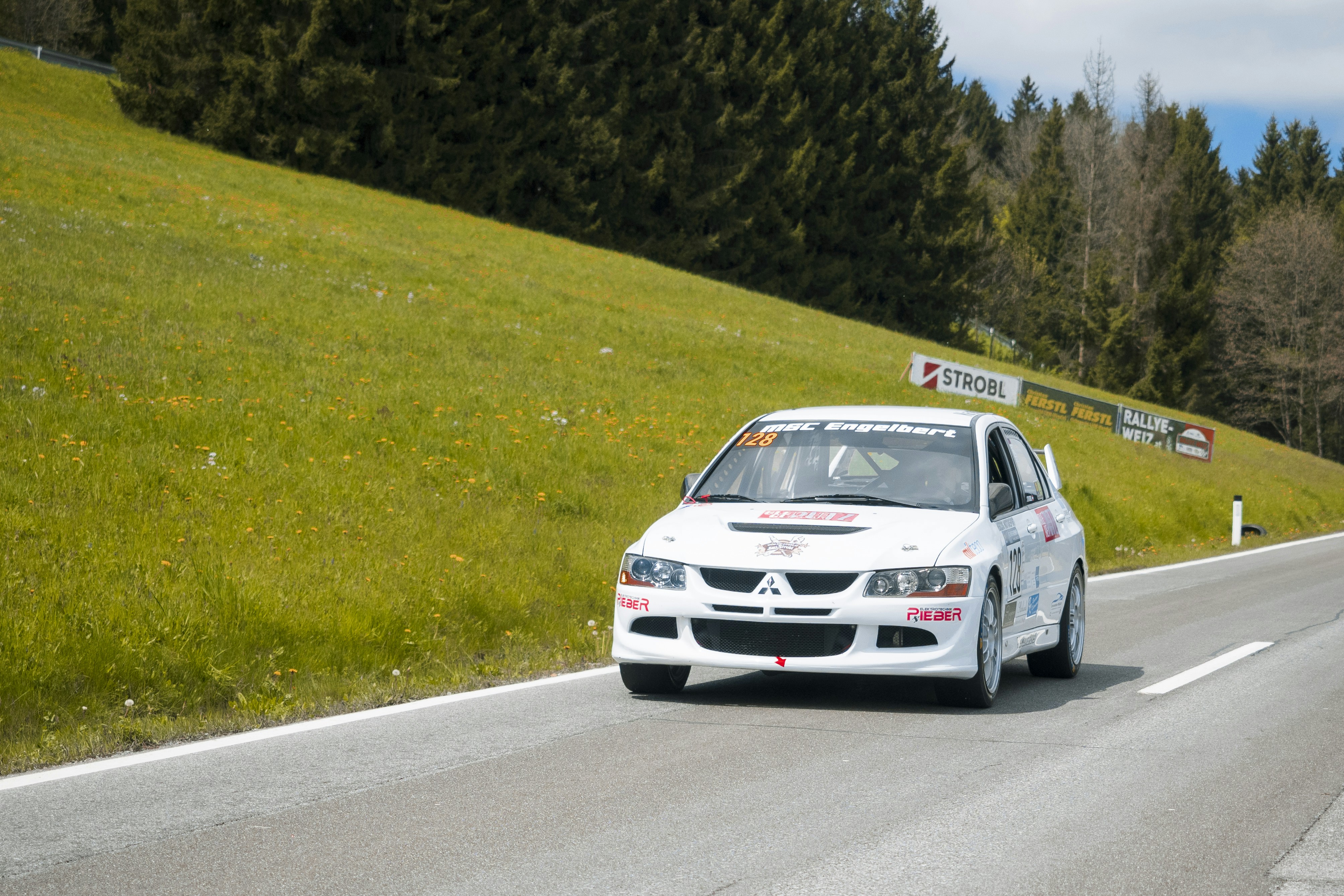 A white race car speeds down a scenic road.