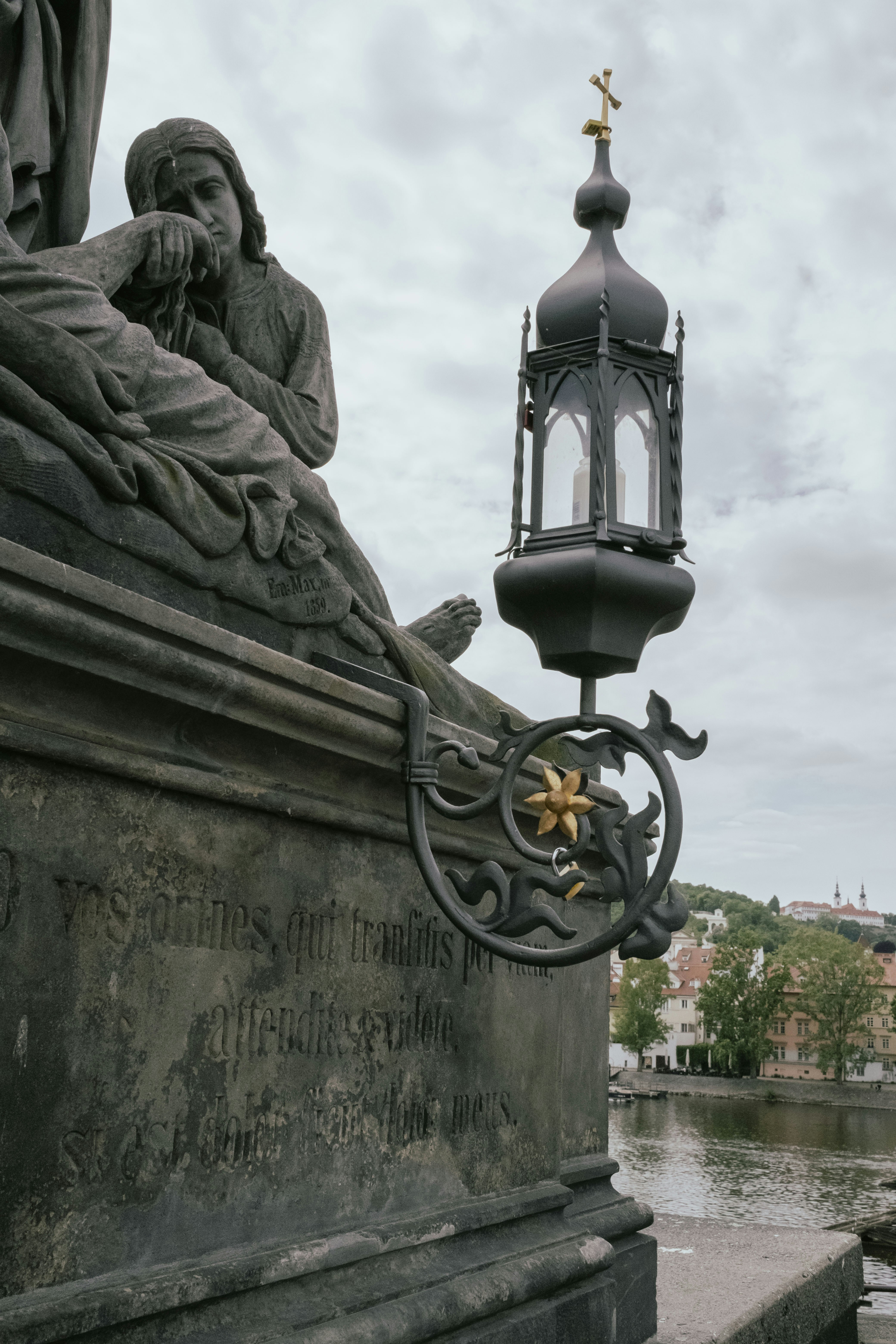 Stone sculpture and lamp post stand on a bridge.