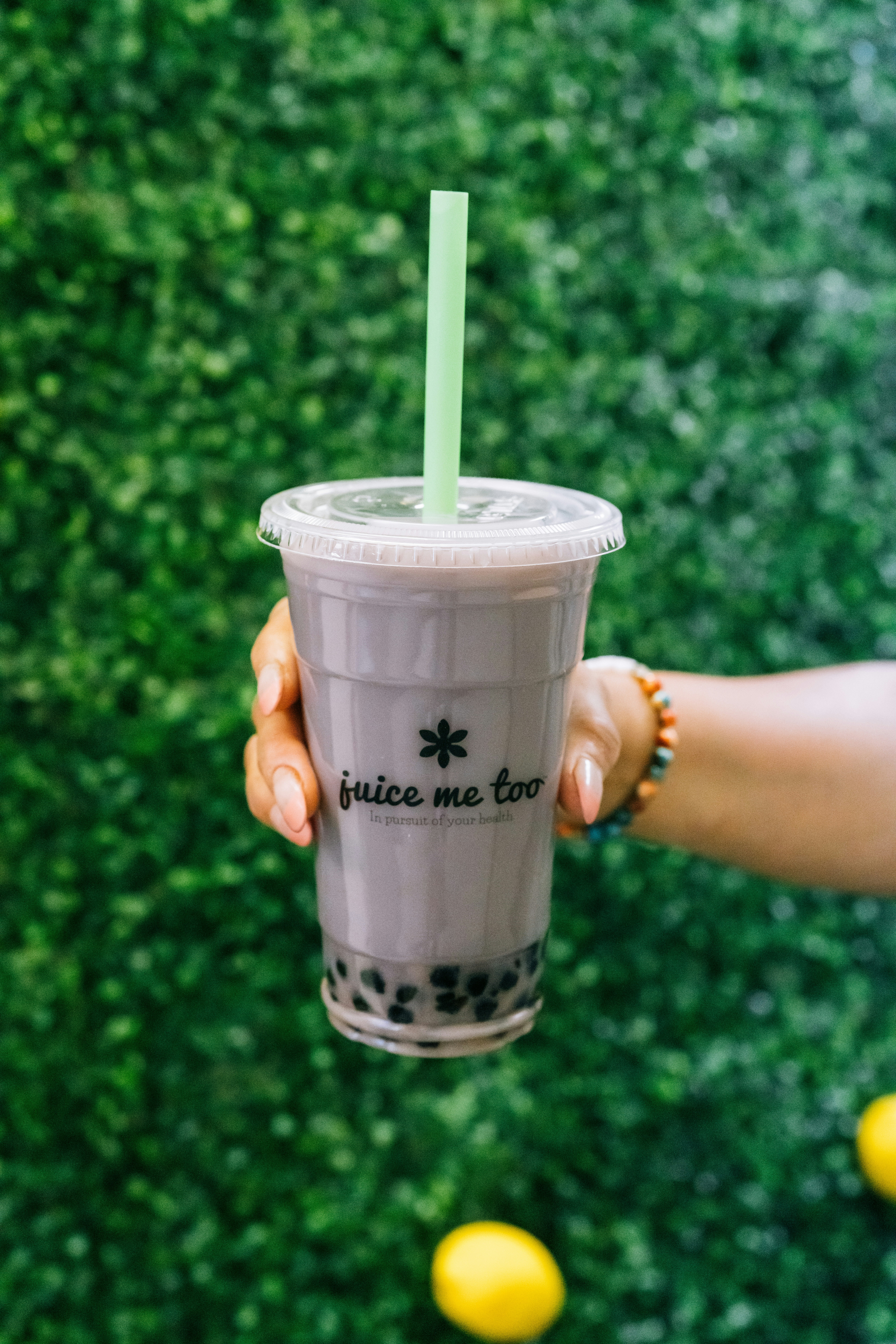 A hand holds a boba drink against a green backdrop.