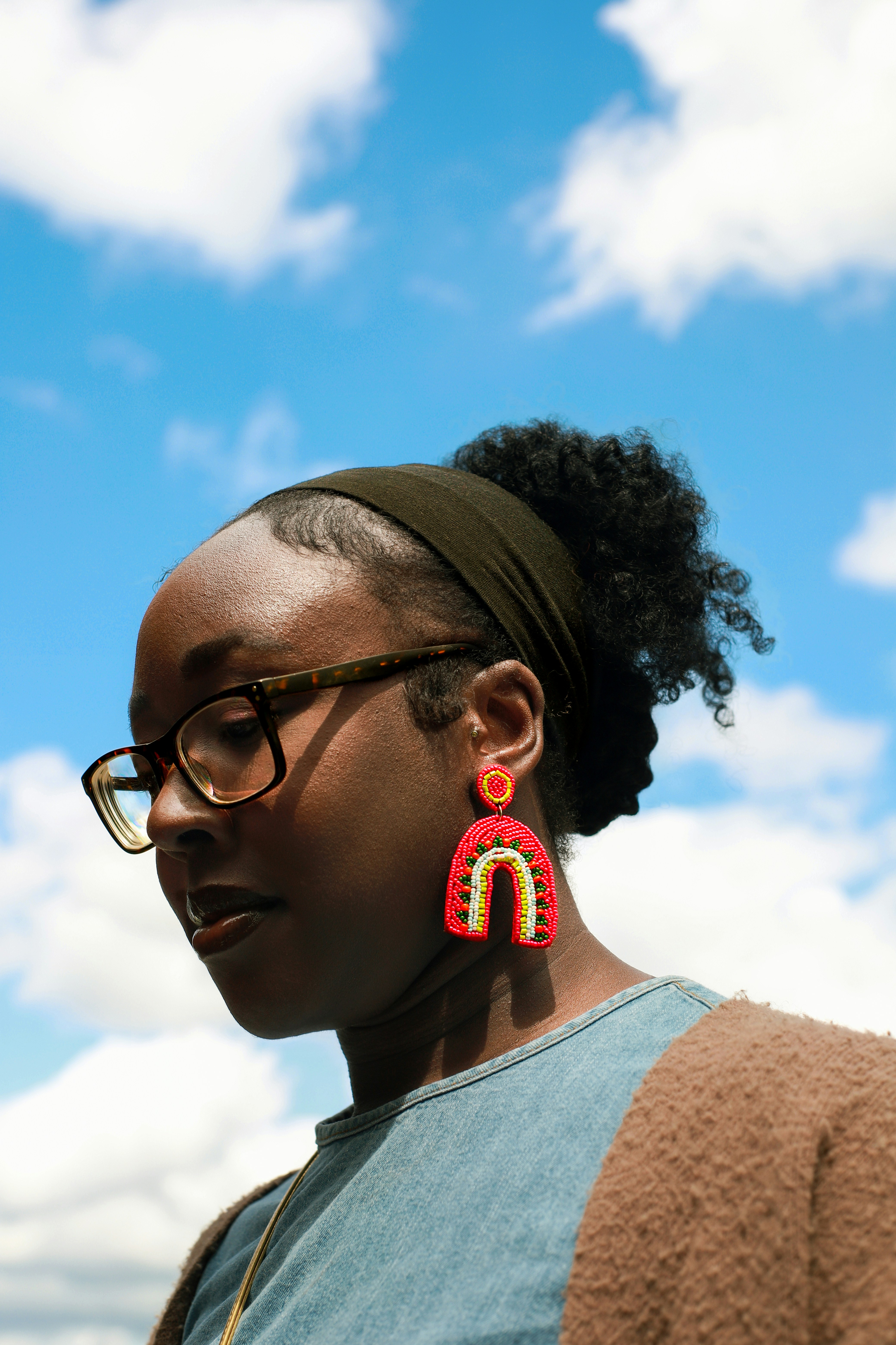 Woman wears rainbow earrings against a blue sky.