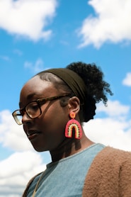 Woman wears rainbow earrings against a blue sky.