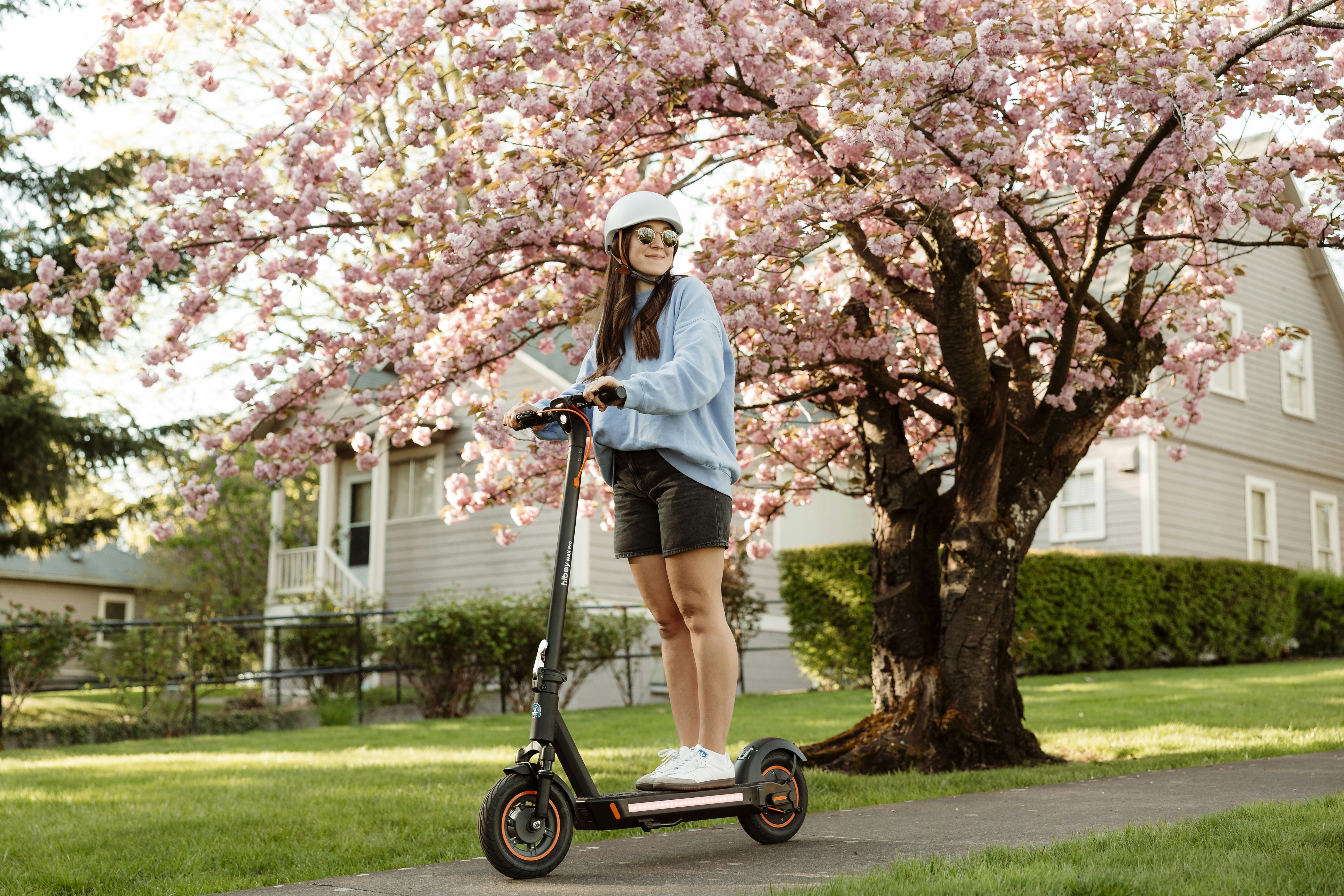 A woman rides a scooter under a cherry blossom tree.