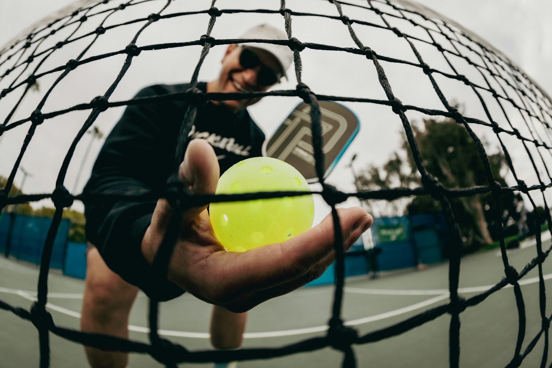 Pickleball player holds a ball with the net in view.