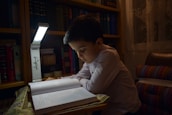 A young boy reads a book in dim light.