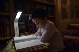 A young boy reads a book in dim light.