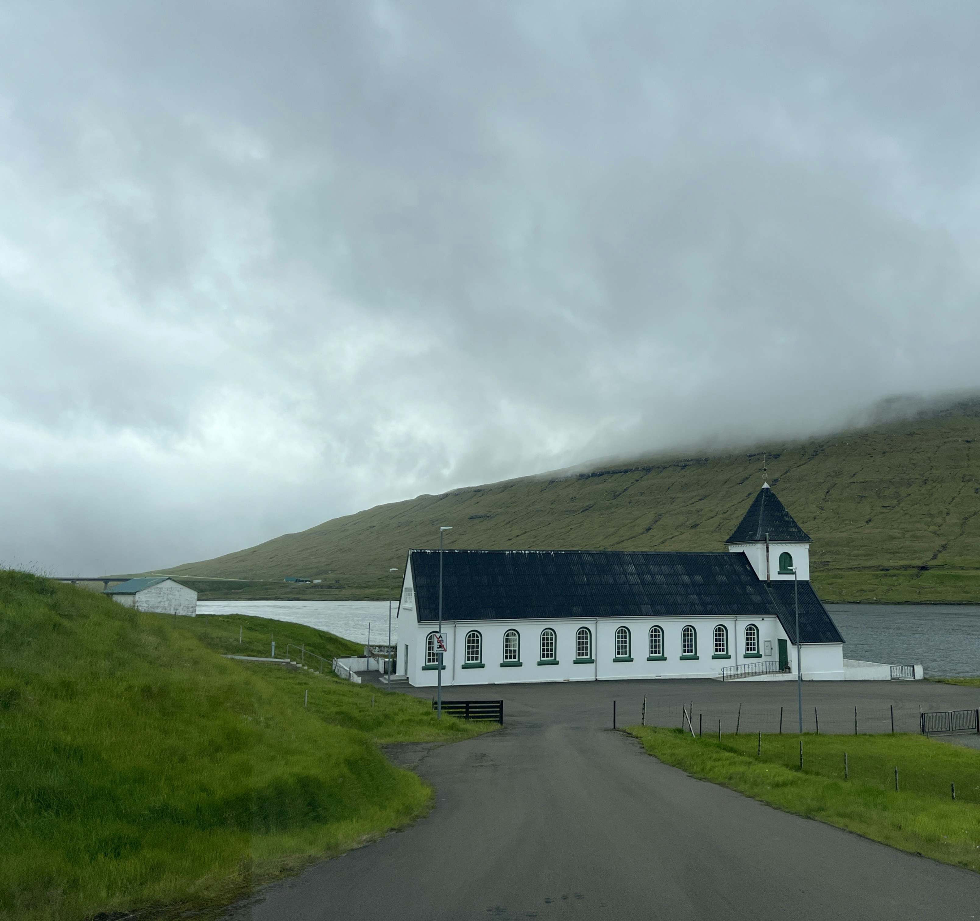 A church sits peacefully by a lake under cloudy skies.
