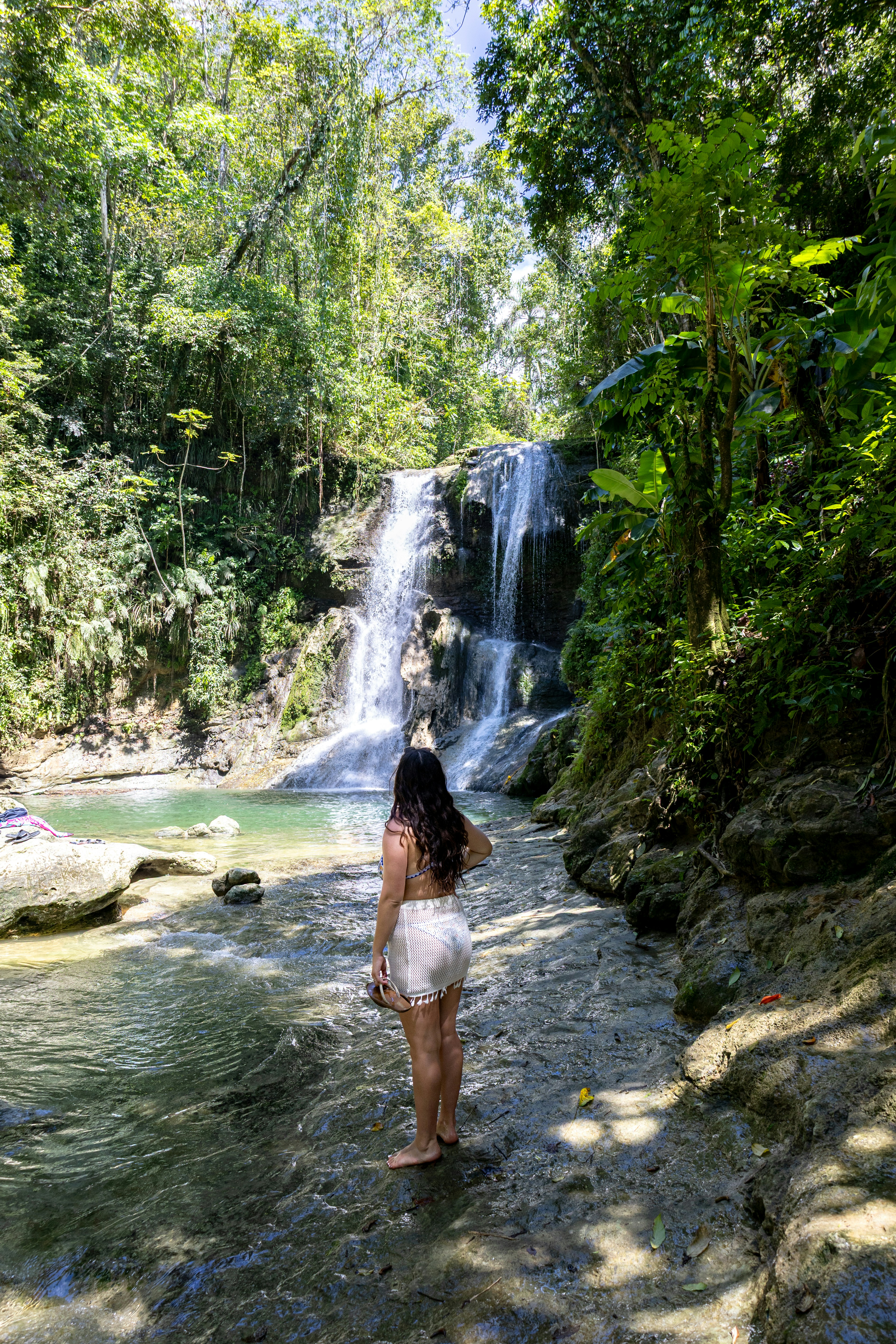 Woman stands before a beautiful jungle waterfall.