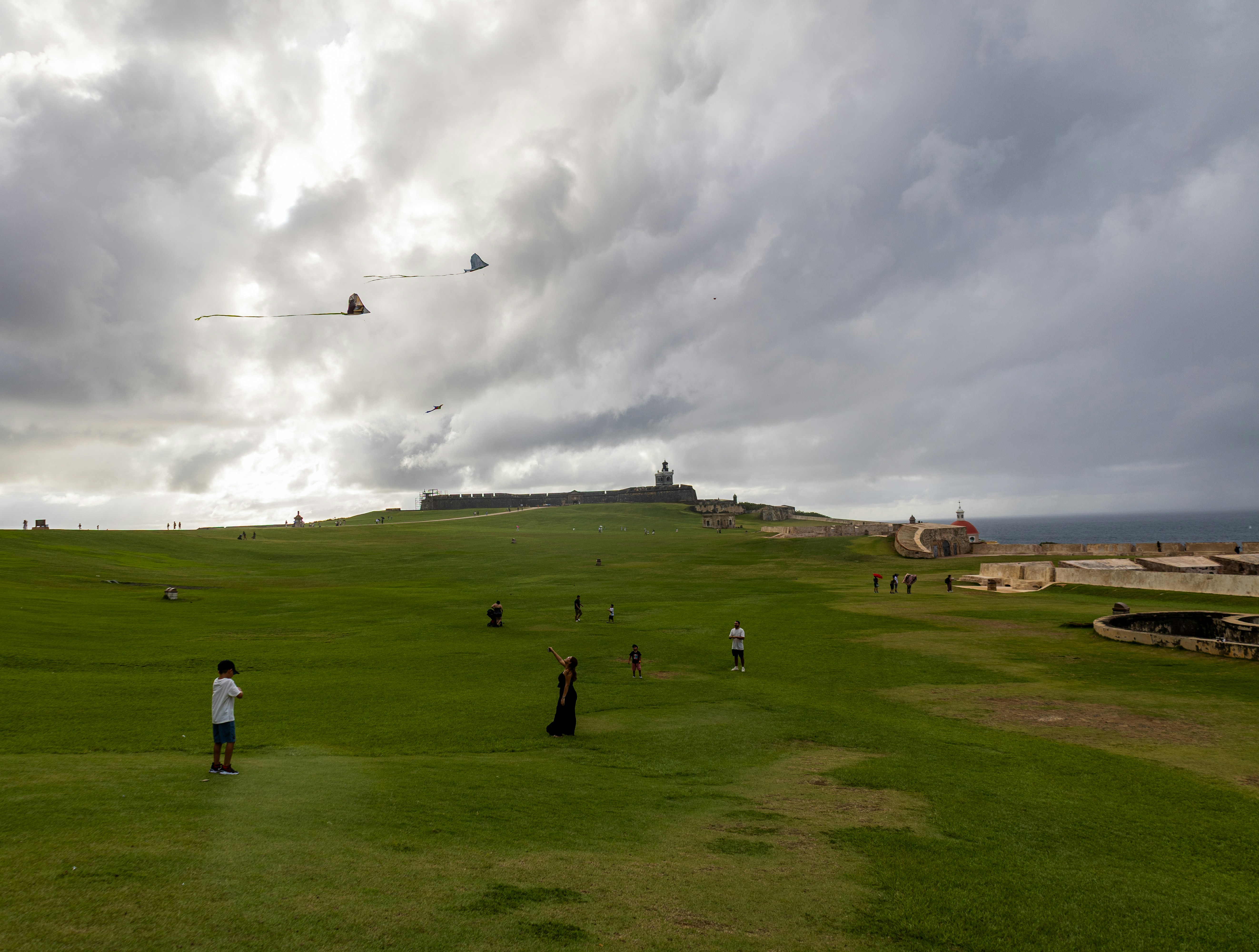 People walk on a grassy hill under a cloudy sky.