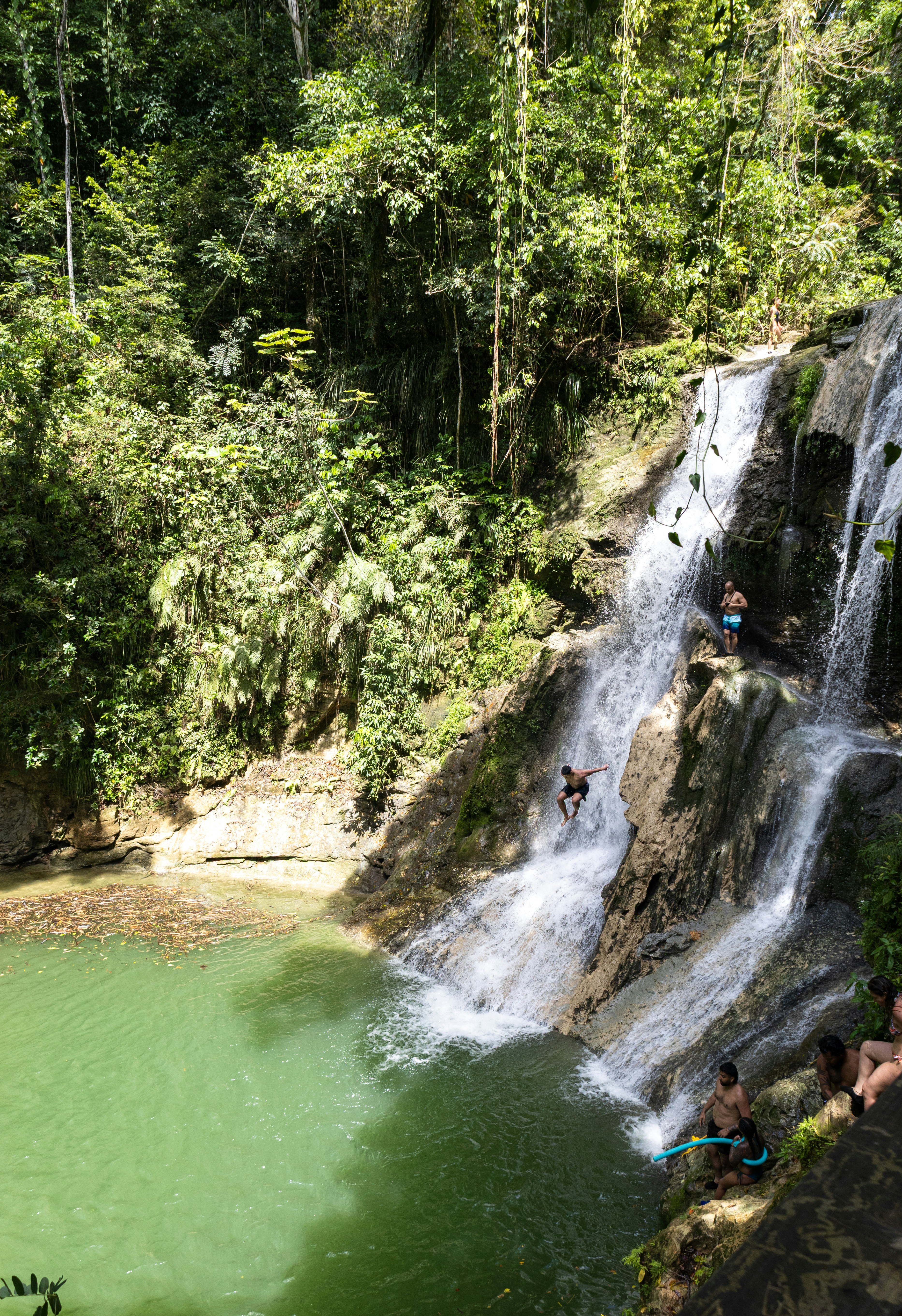 People are swimming and playing in a waterfall.
