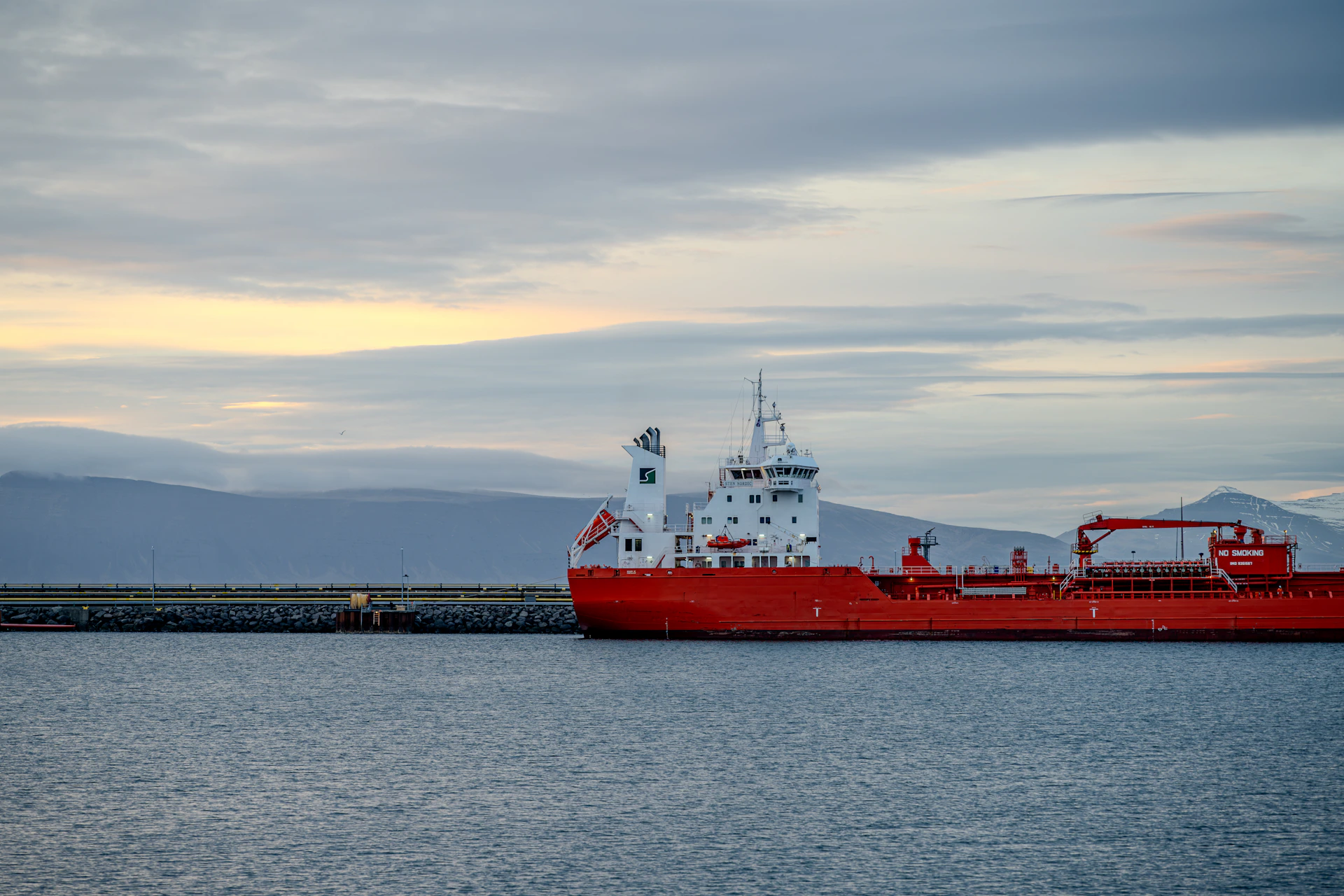 A red ship floats near a breakwater