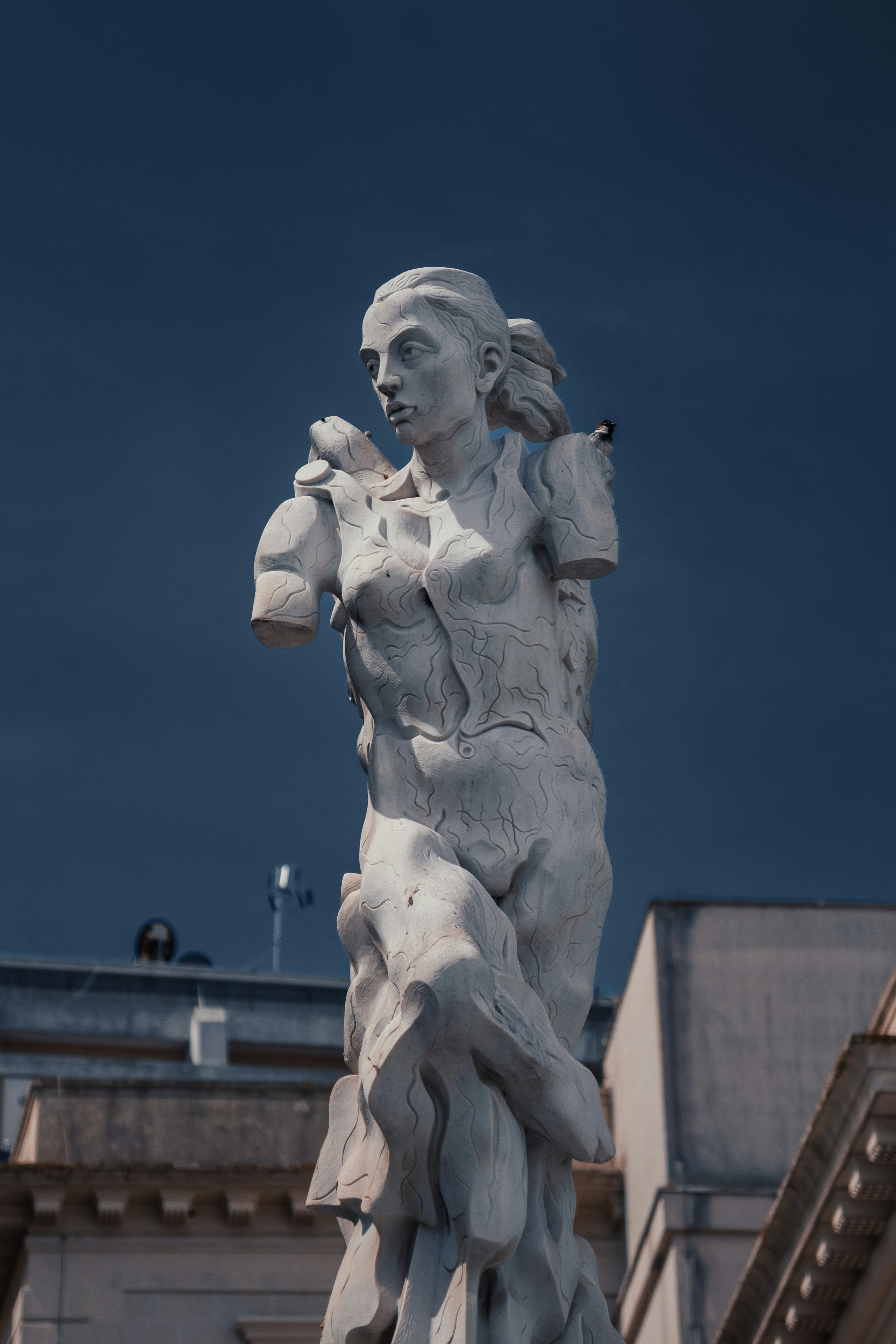 A damaged statue stands against a dark sky.