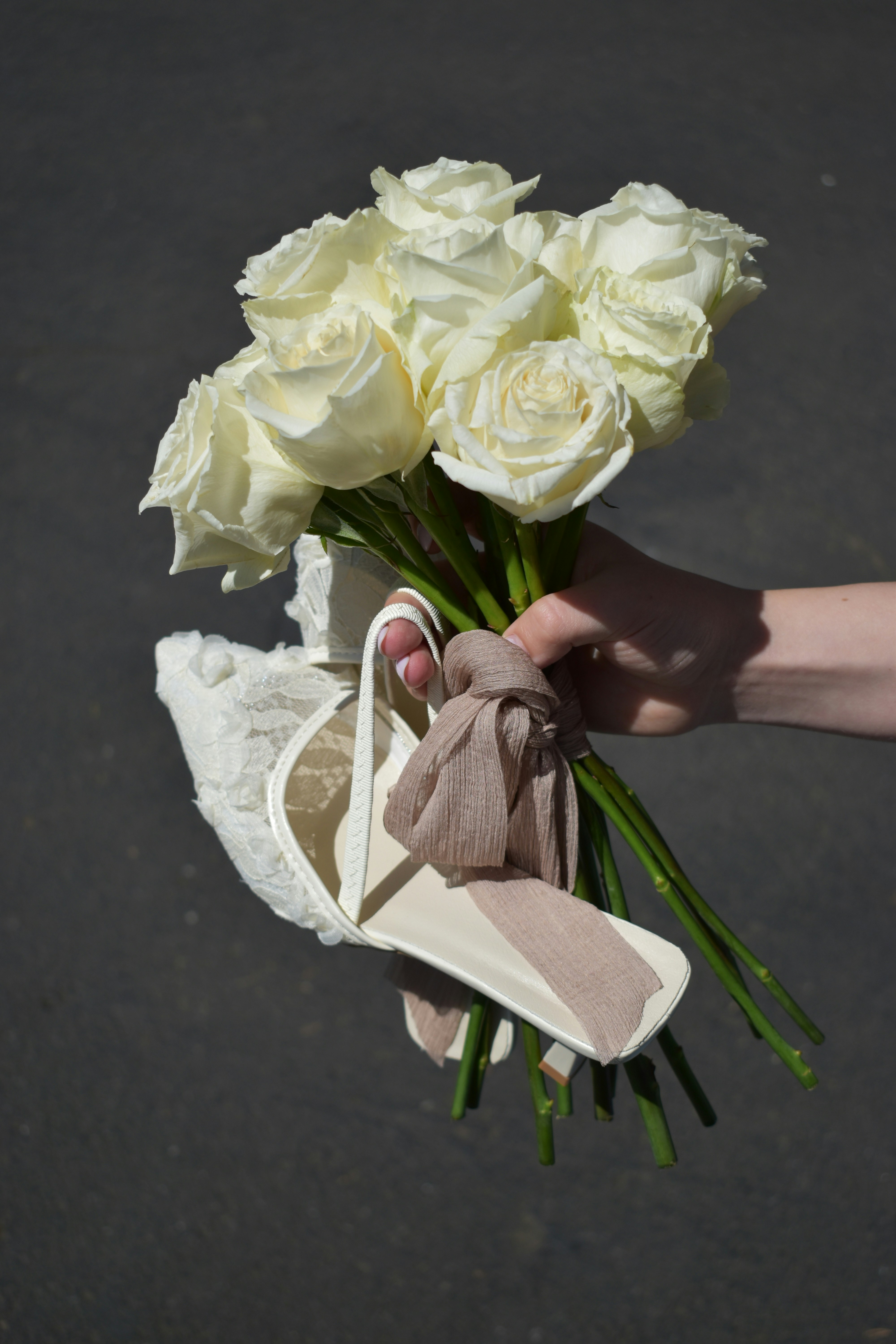 Hand holding a bouquet of white roses and a shoe.