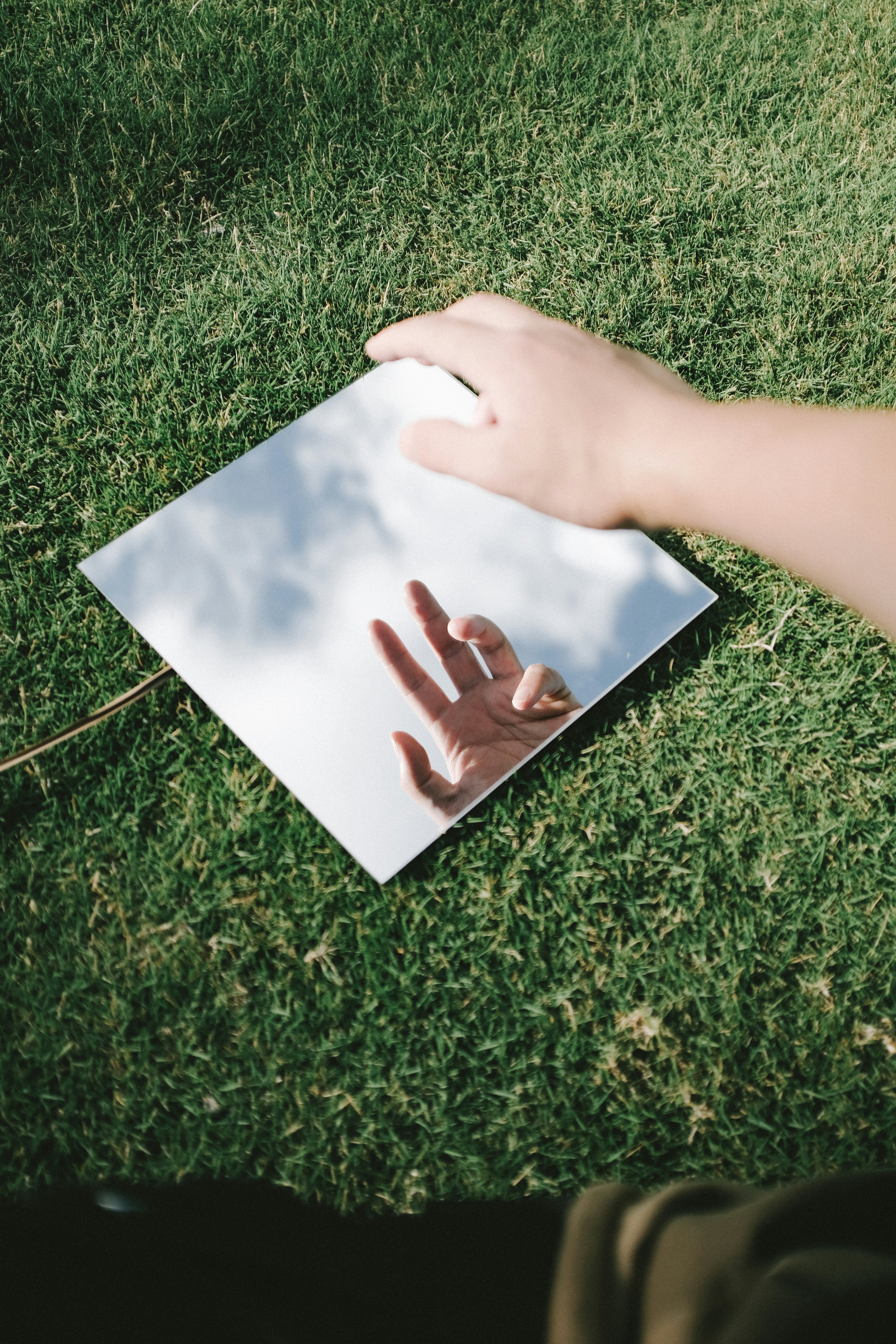 A hand reflects in a mirror on grass