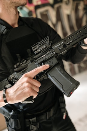 Man holds a rifle with a large magazine.