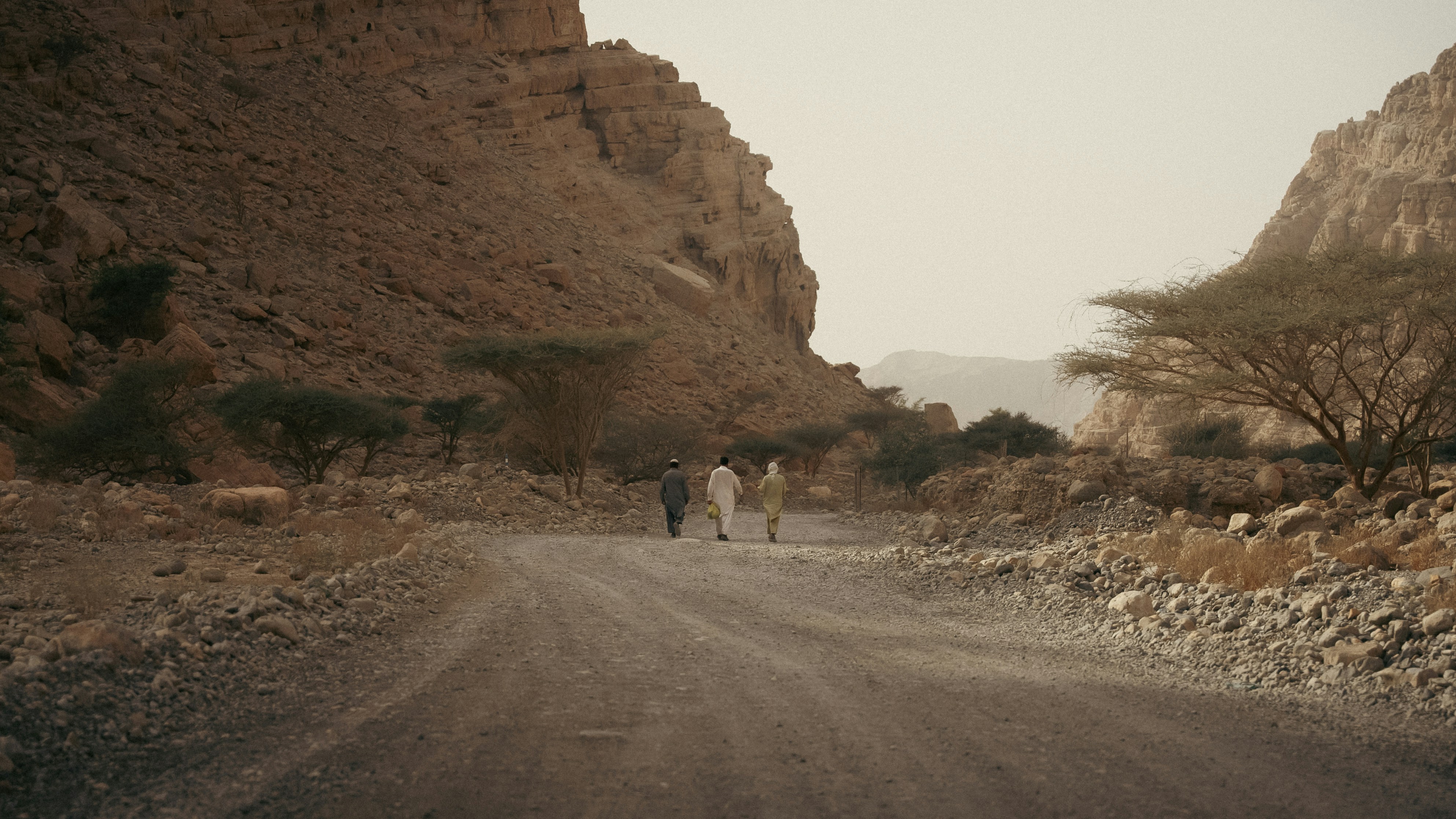 Three people walk down a dusty road in a canyon.