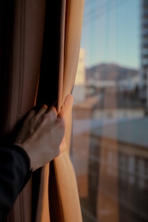 A hand pulls back a curtain to reveal the view.