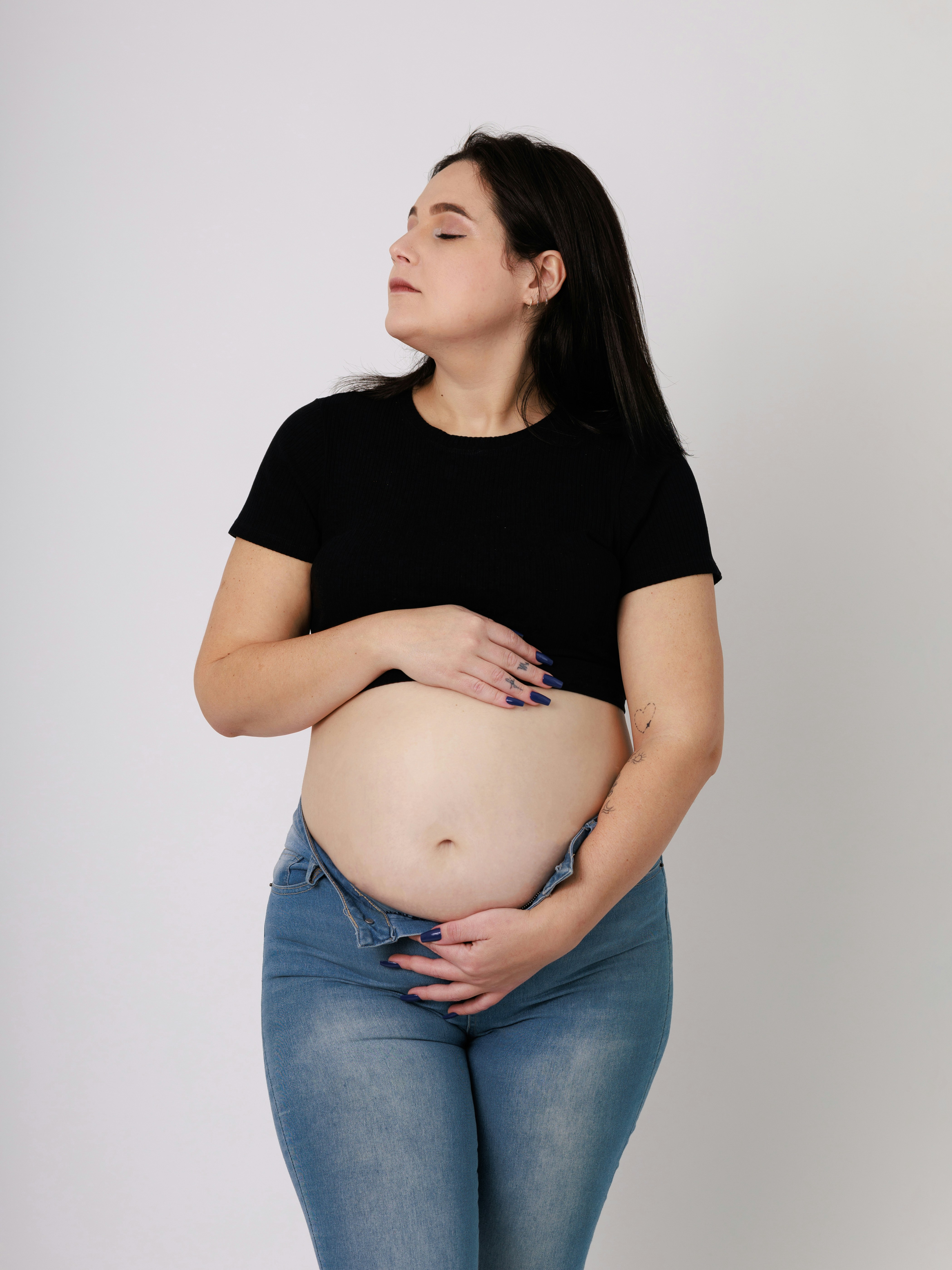 A woman holds her stomach with her jeans undone.