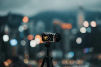 A mirrorless camera on a tripod facing a city skyline at blue hour, its lights just coming on