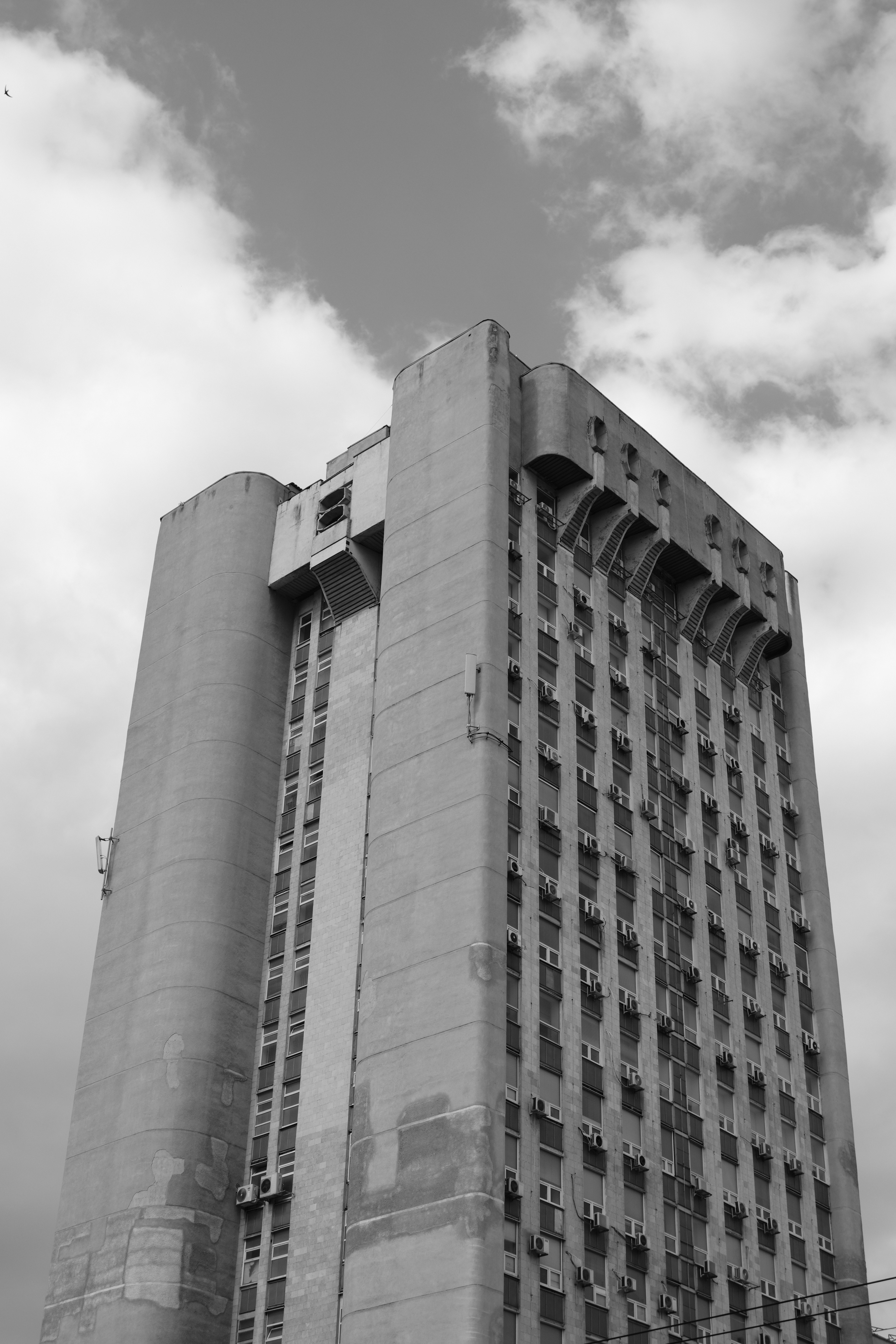 A tall building reaches up towards cloudy skies.
