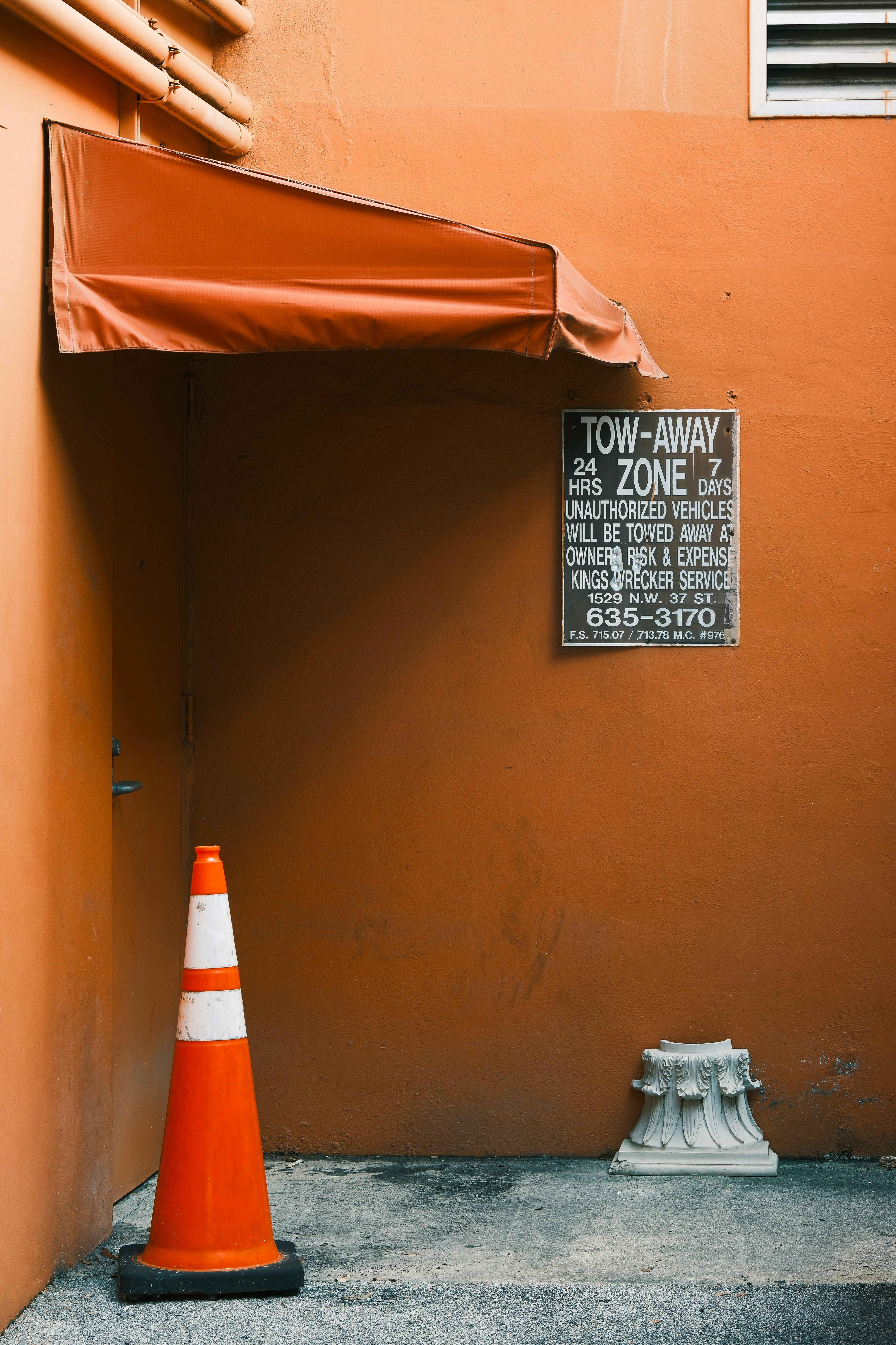 Mur orange avec un cône de signalisation et un panneau.