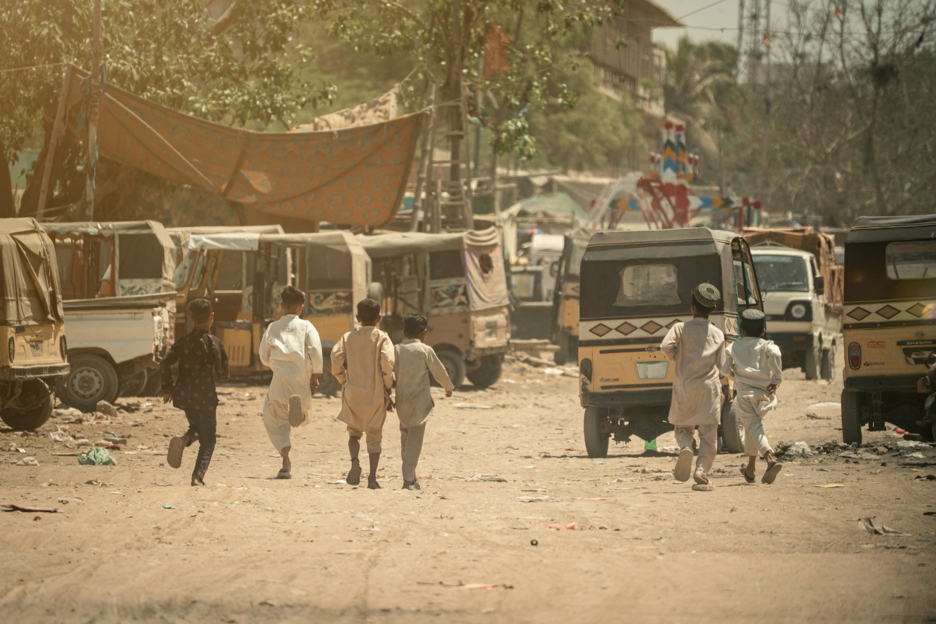 Children run in a dusty street near vehicles.