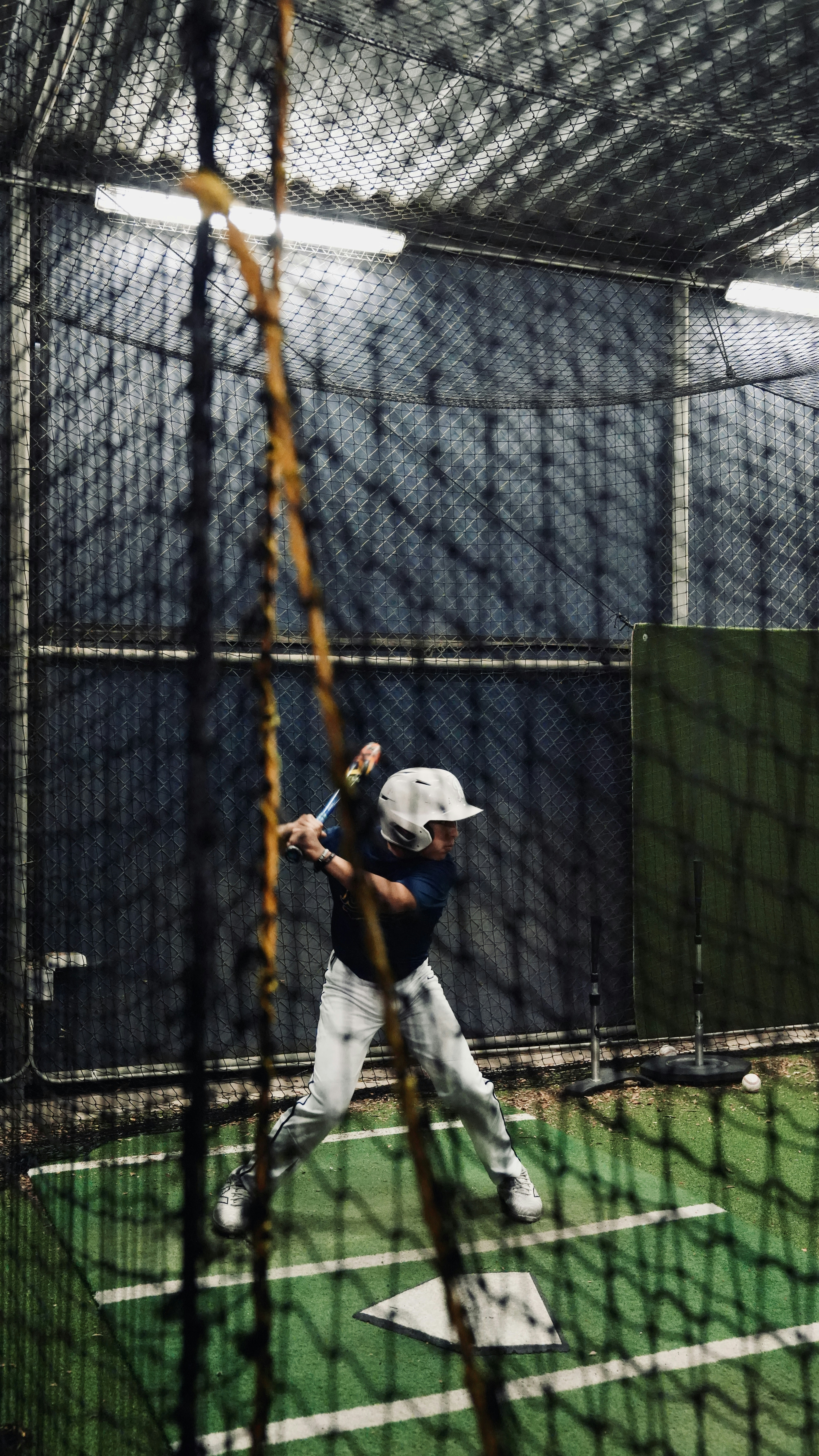 A baseball player swings in a batting cage.