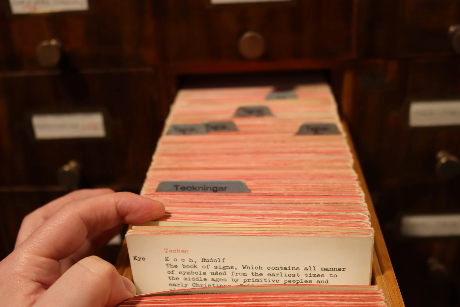 A hand pulls a card from the library's card catalog