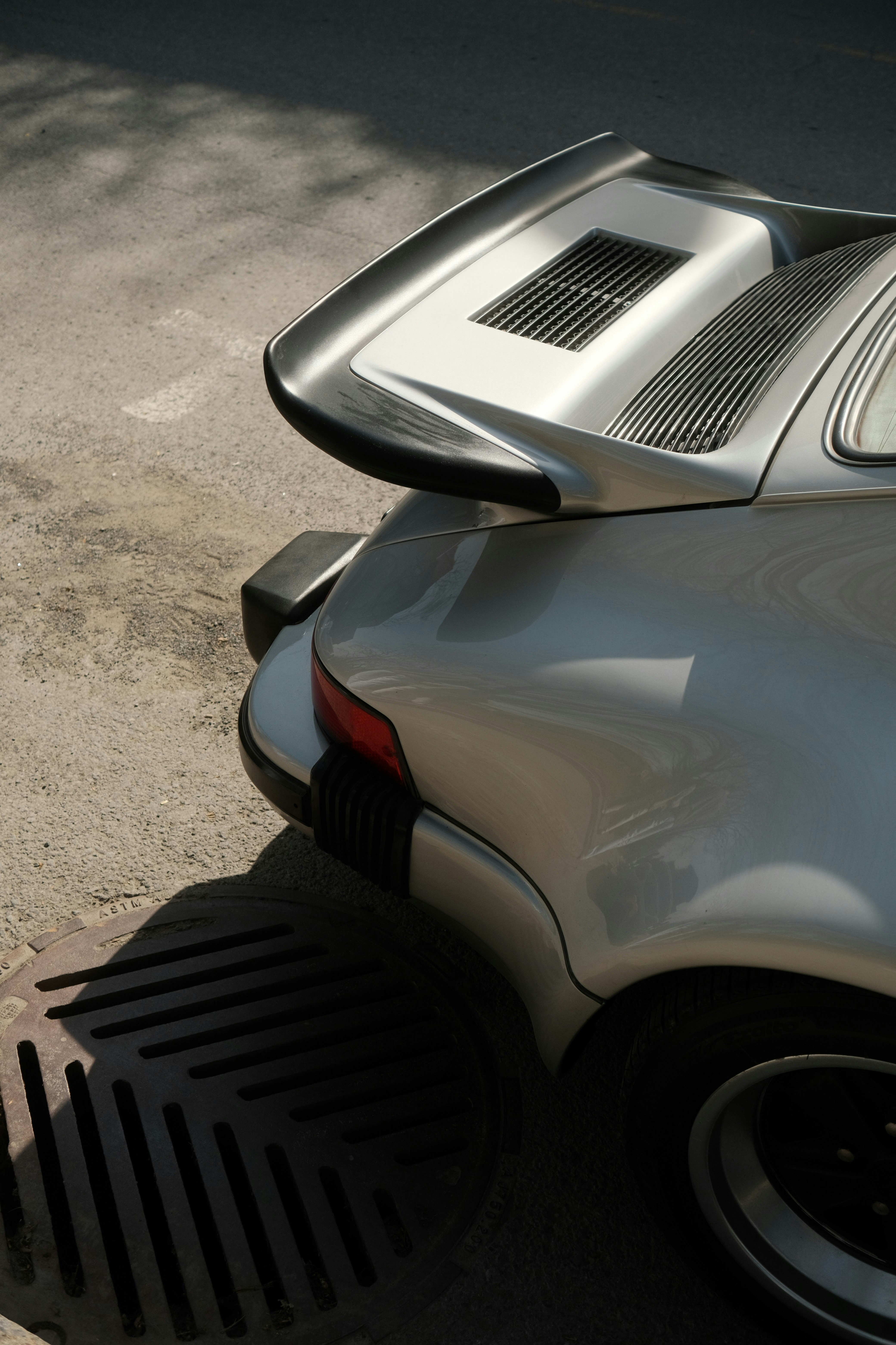A silver porsche sports car shows its spoiler.