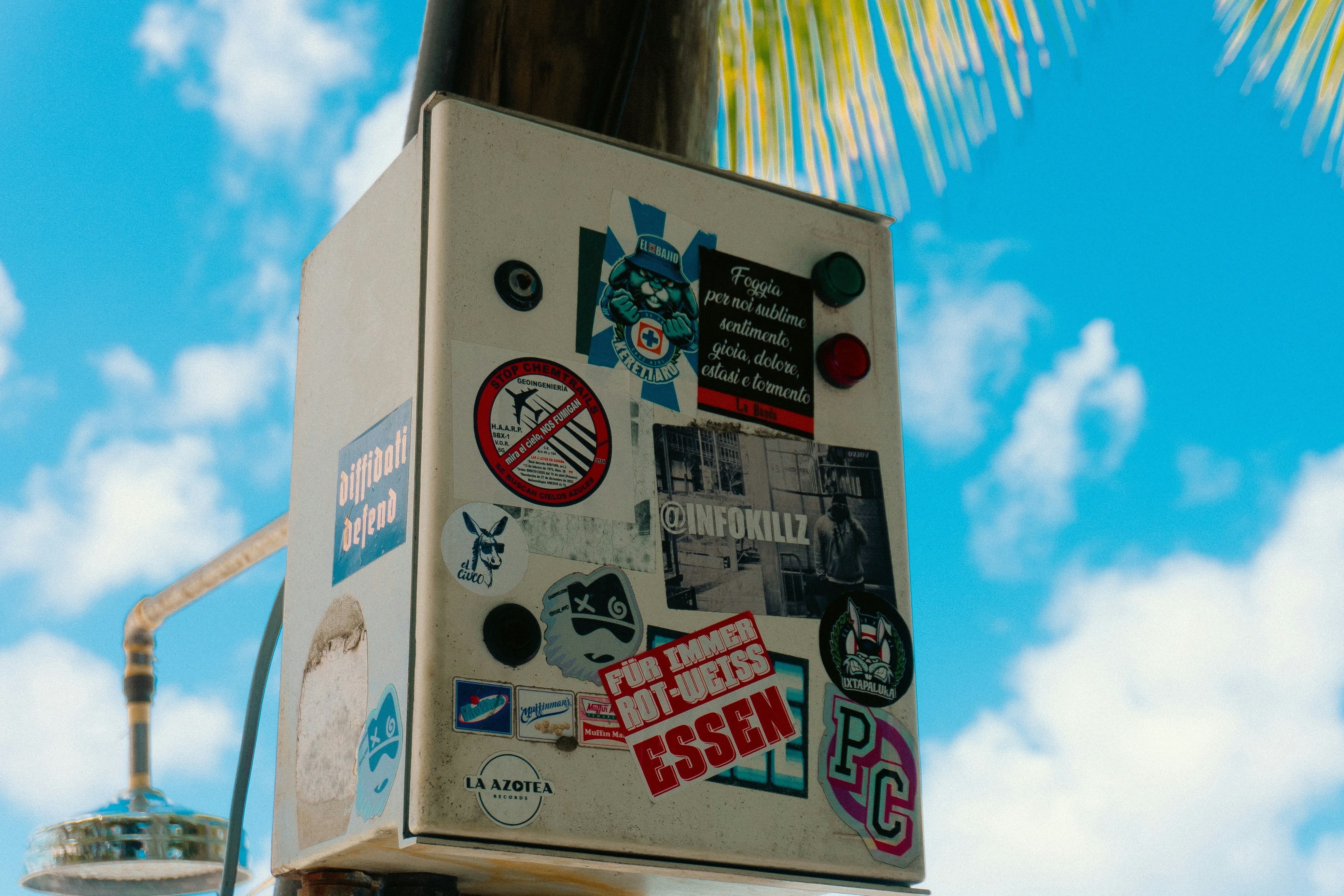 A box covered in stickers stands against the blue sky.