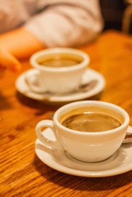 Two cups of coffee sit on a wooden table.
