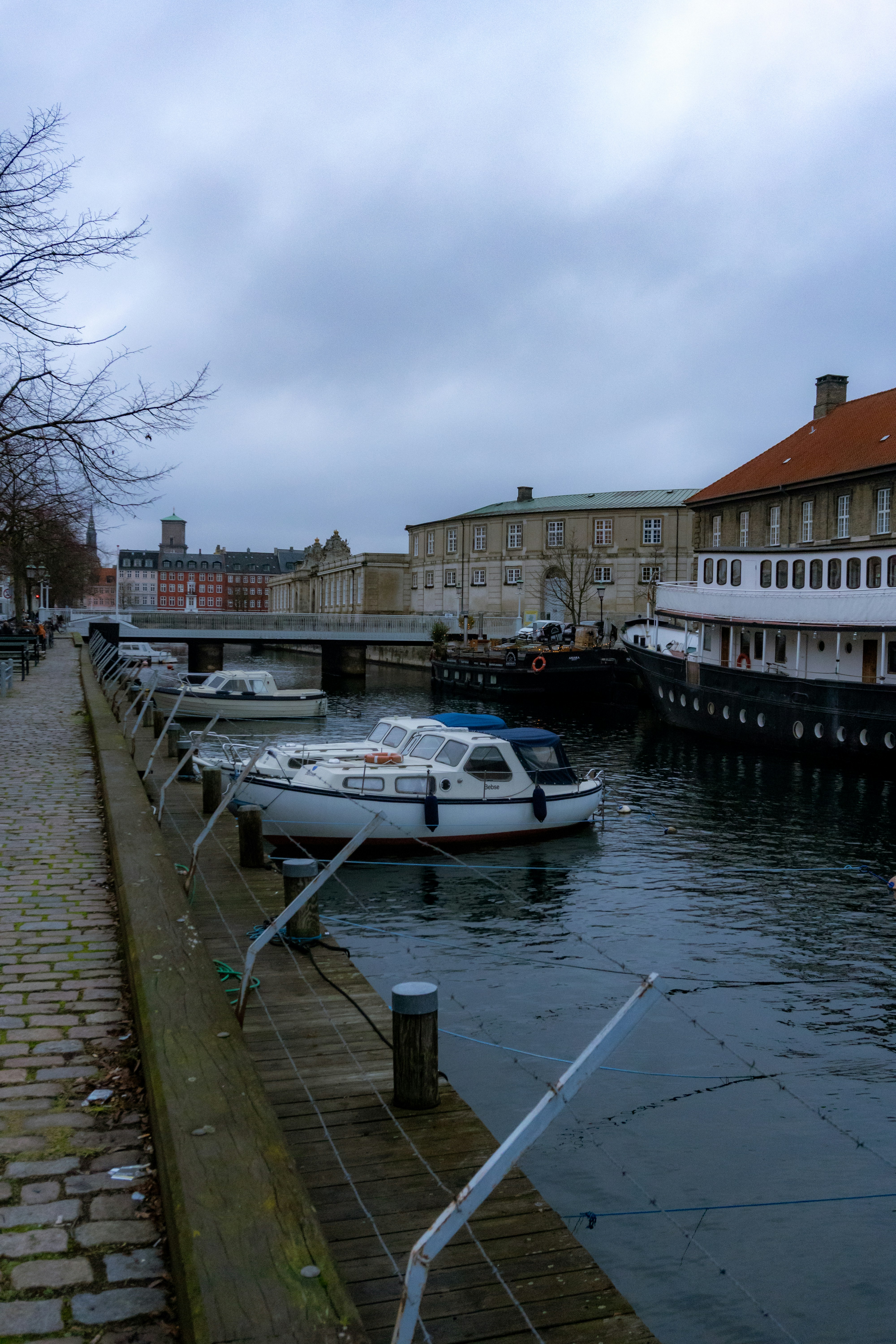 Boats are docked along a canal on a cloudy day.