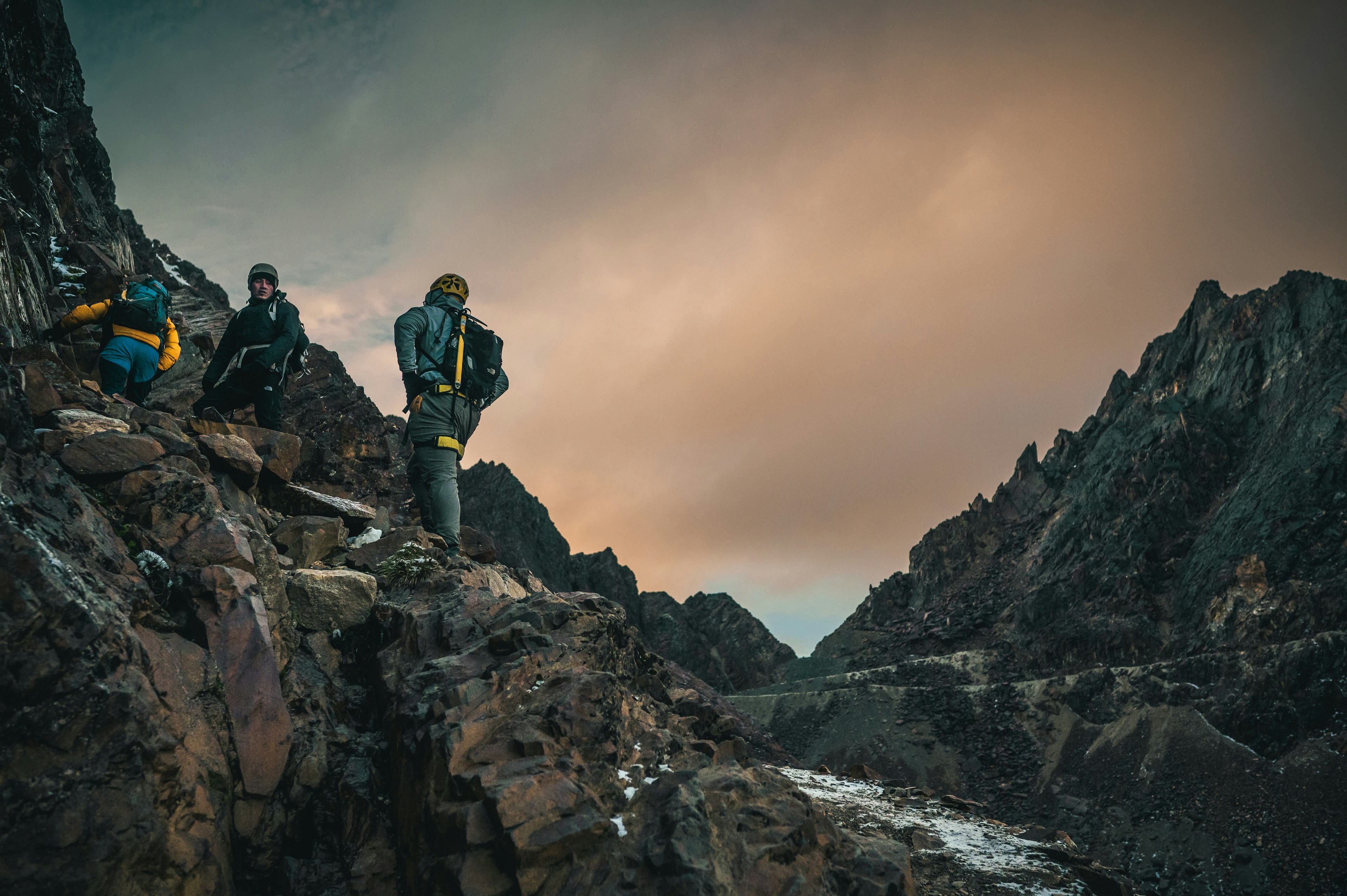 Abenteurer erklimmen unter bewölktem Himmel einen felsigen Berg.