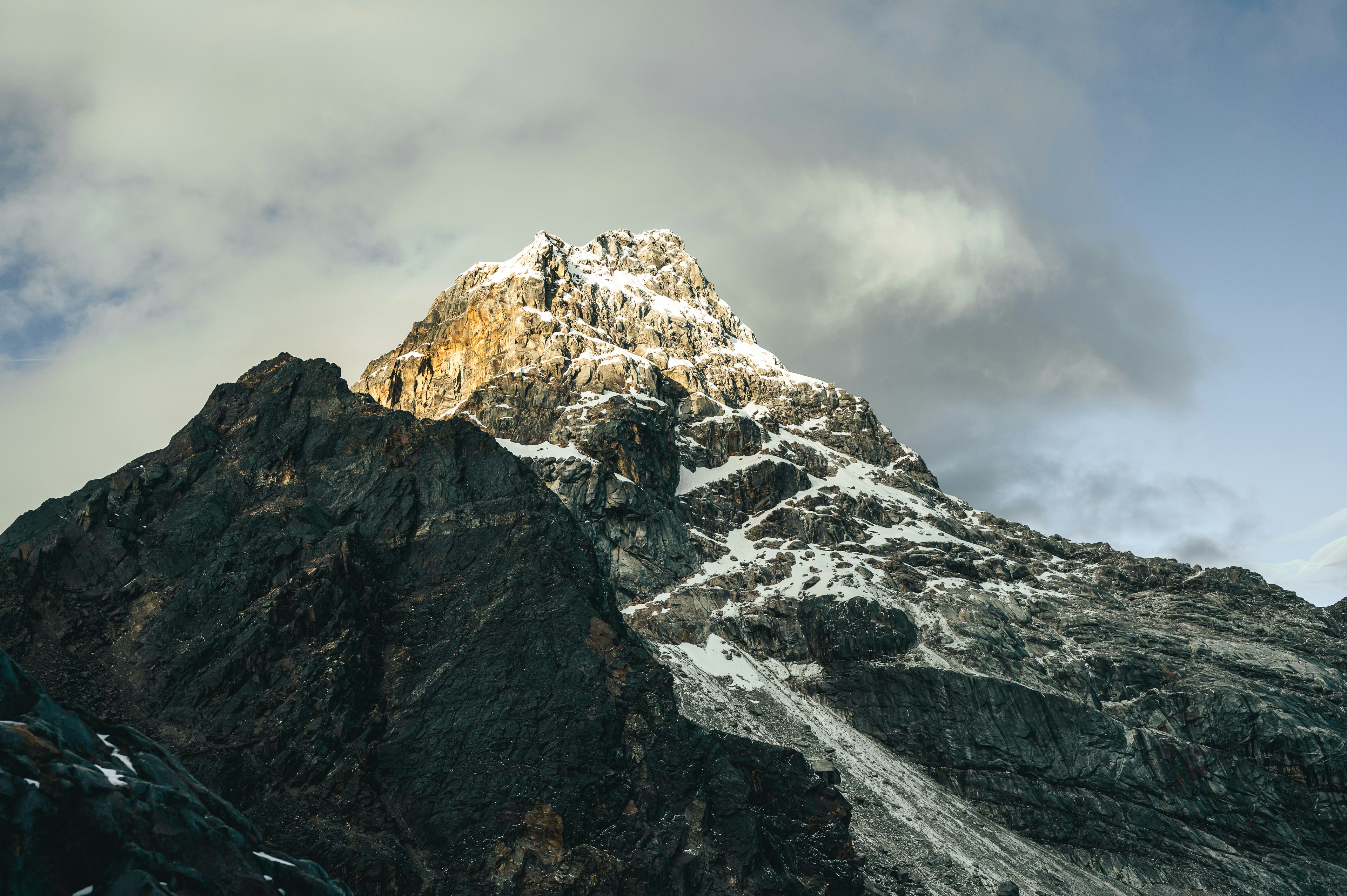 Ein schneebedeckter Berggipfel durchdringt den wolkenverhangenen Himmel.