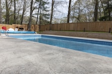 A backyard pool with wood fence and trees.