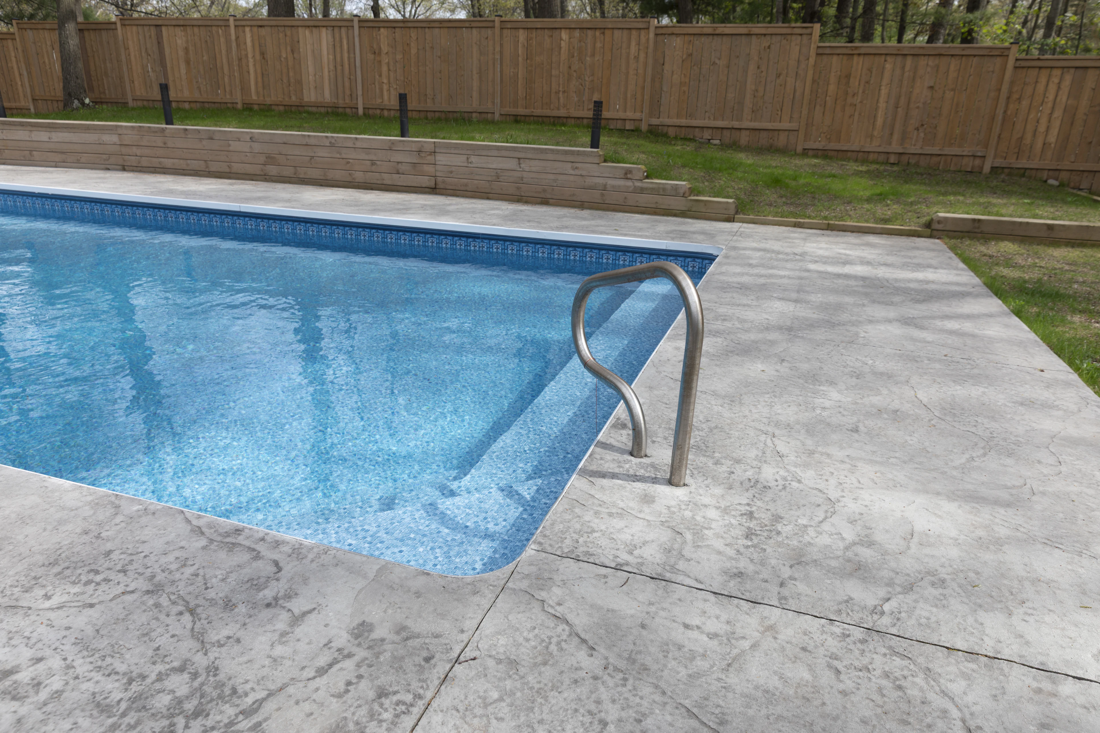 Backyard pool framed by light stone coping and travertine-style pavers