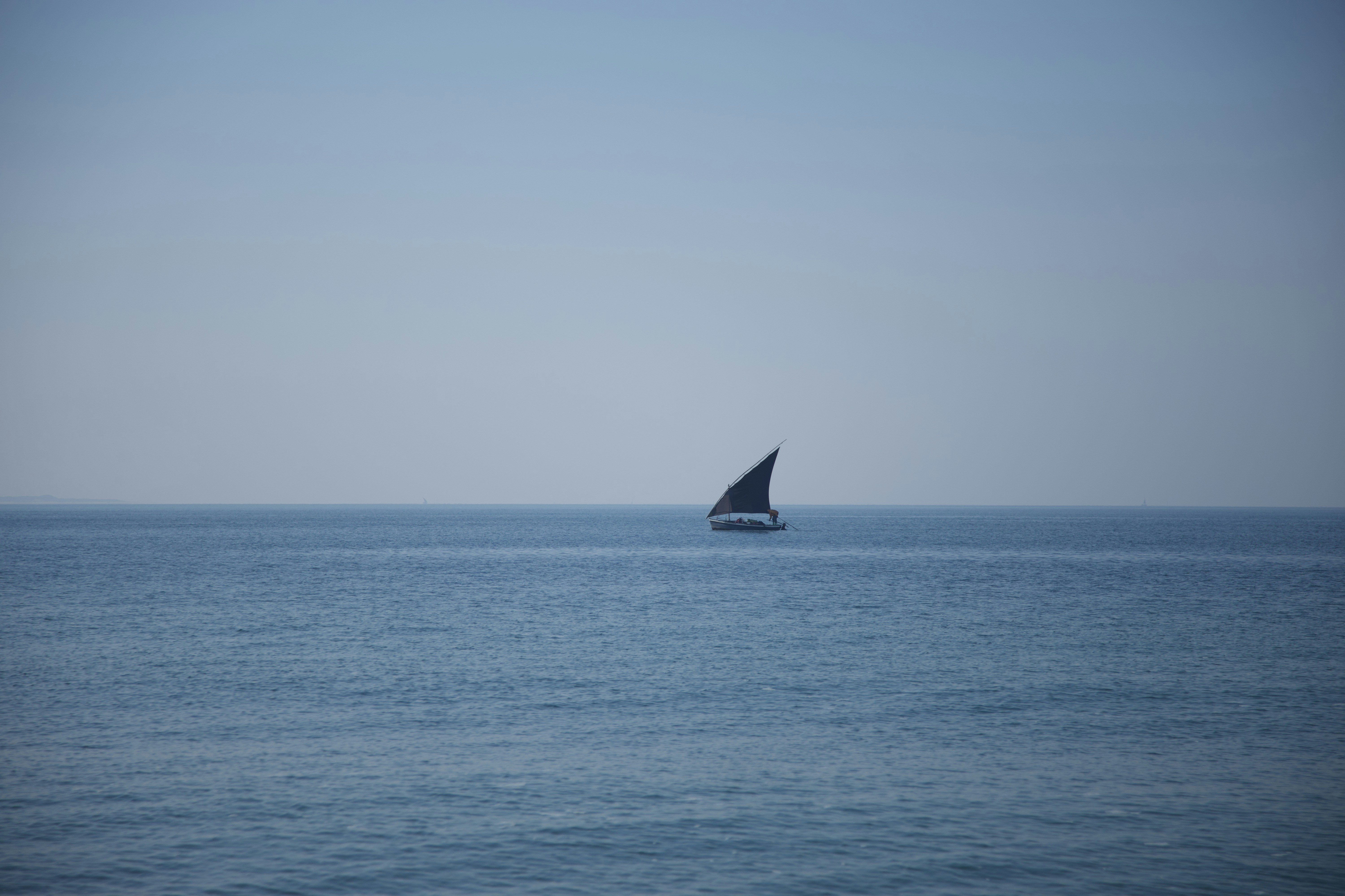 A sailboat glides across the vast, calm ocean.