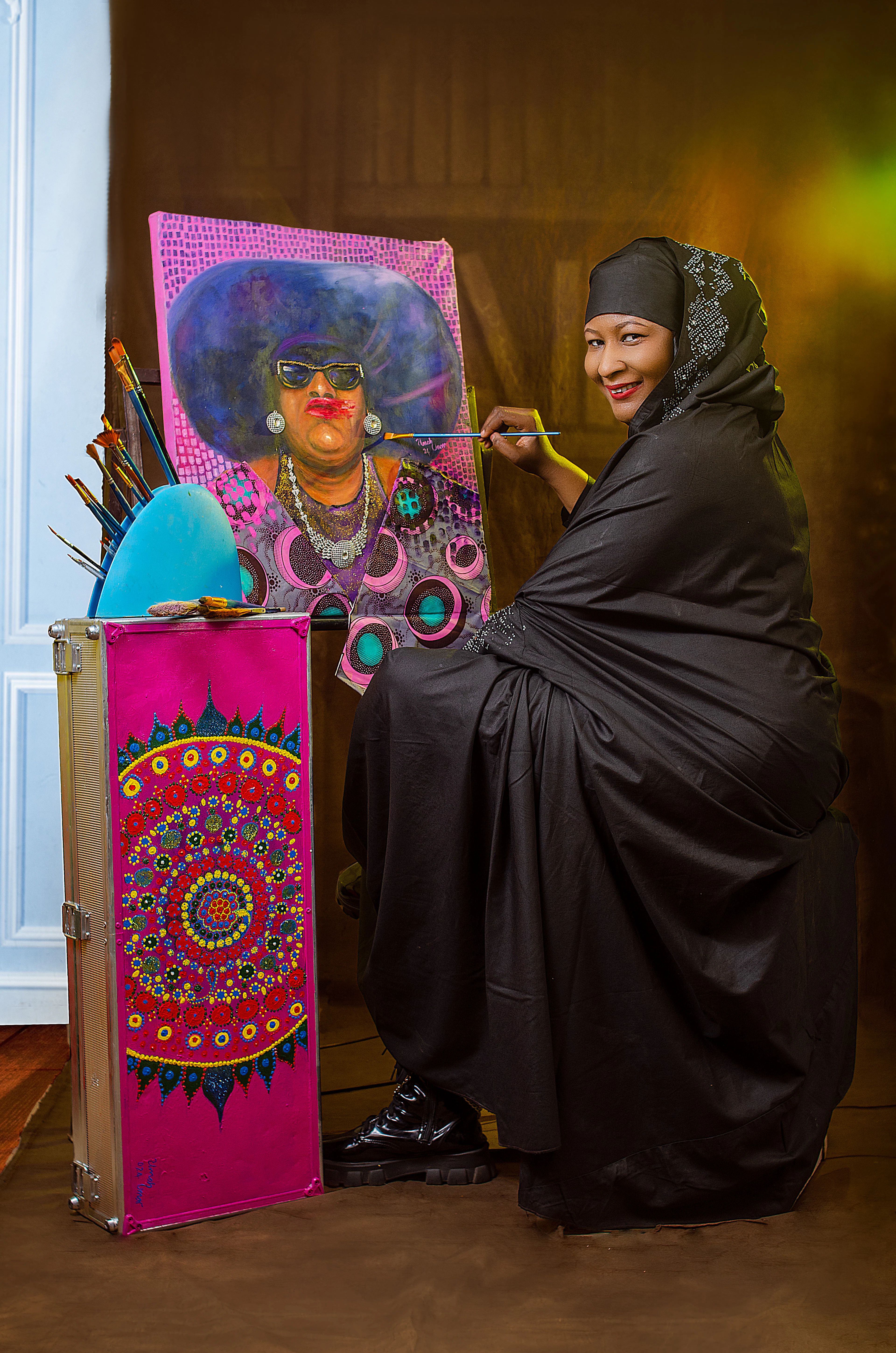 An artist in her studio beside a colourful portrait she painted
