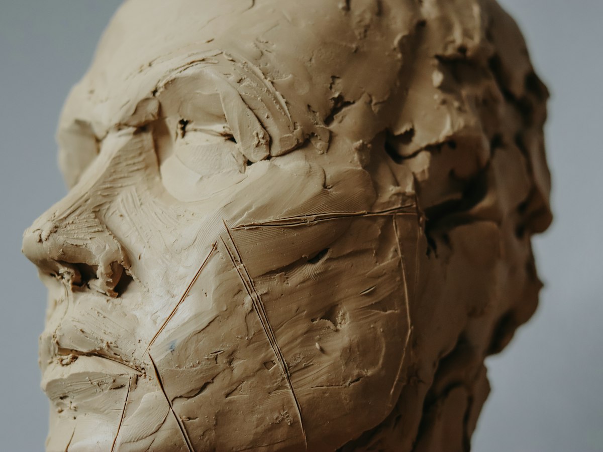 Gros plan sur une tête sculptée en argile brute, vue de profil, avec les traces d'outils visibles