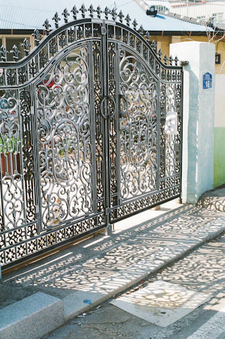 Ornate wrought-iron gates cast shadows on the pavement.