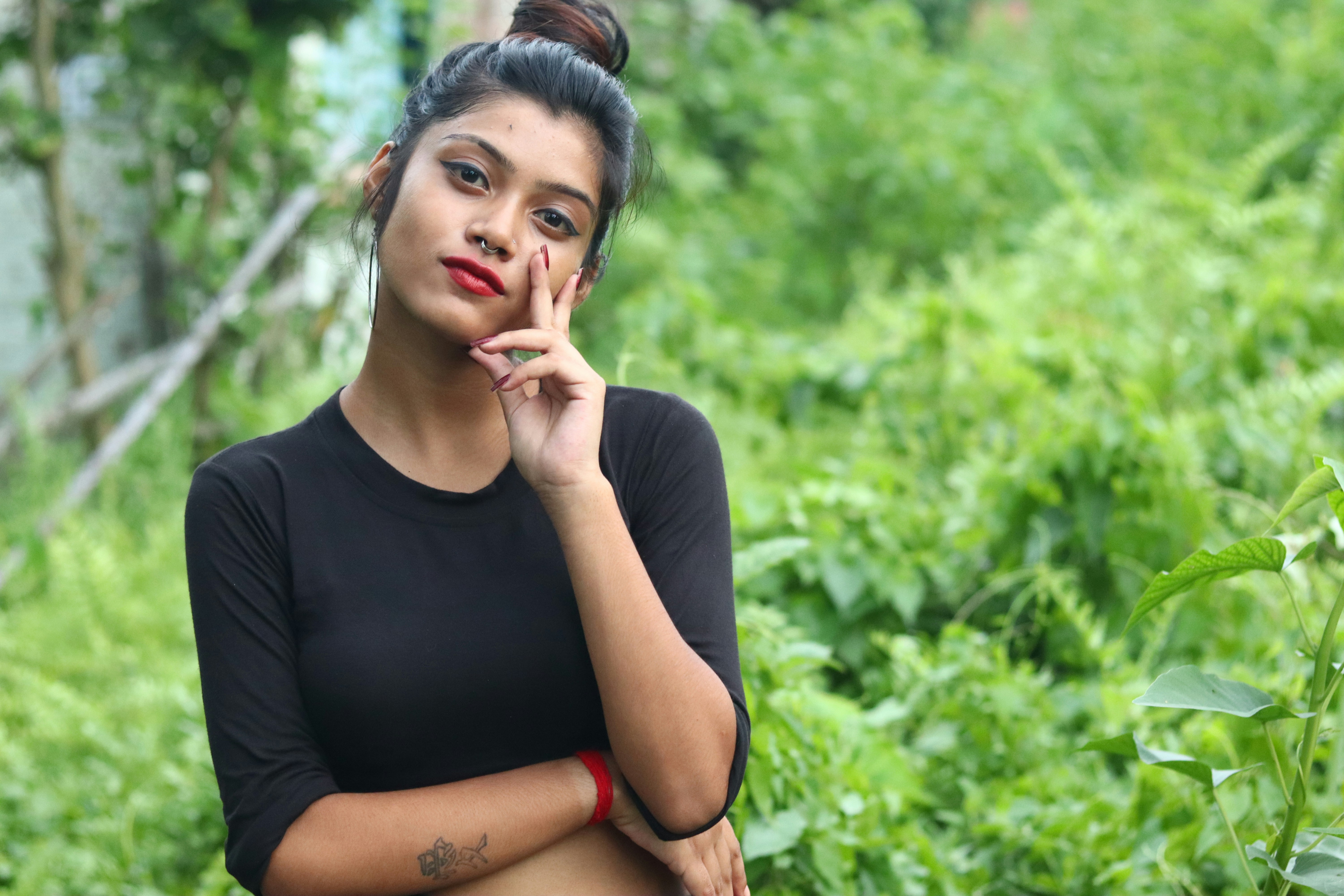 A young woman poses thoughtfully amidst greenery.