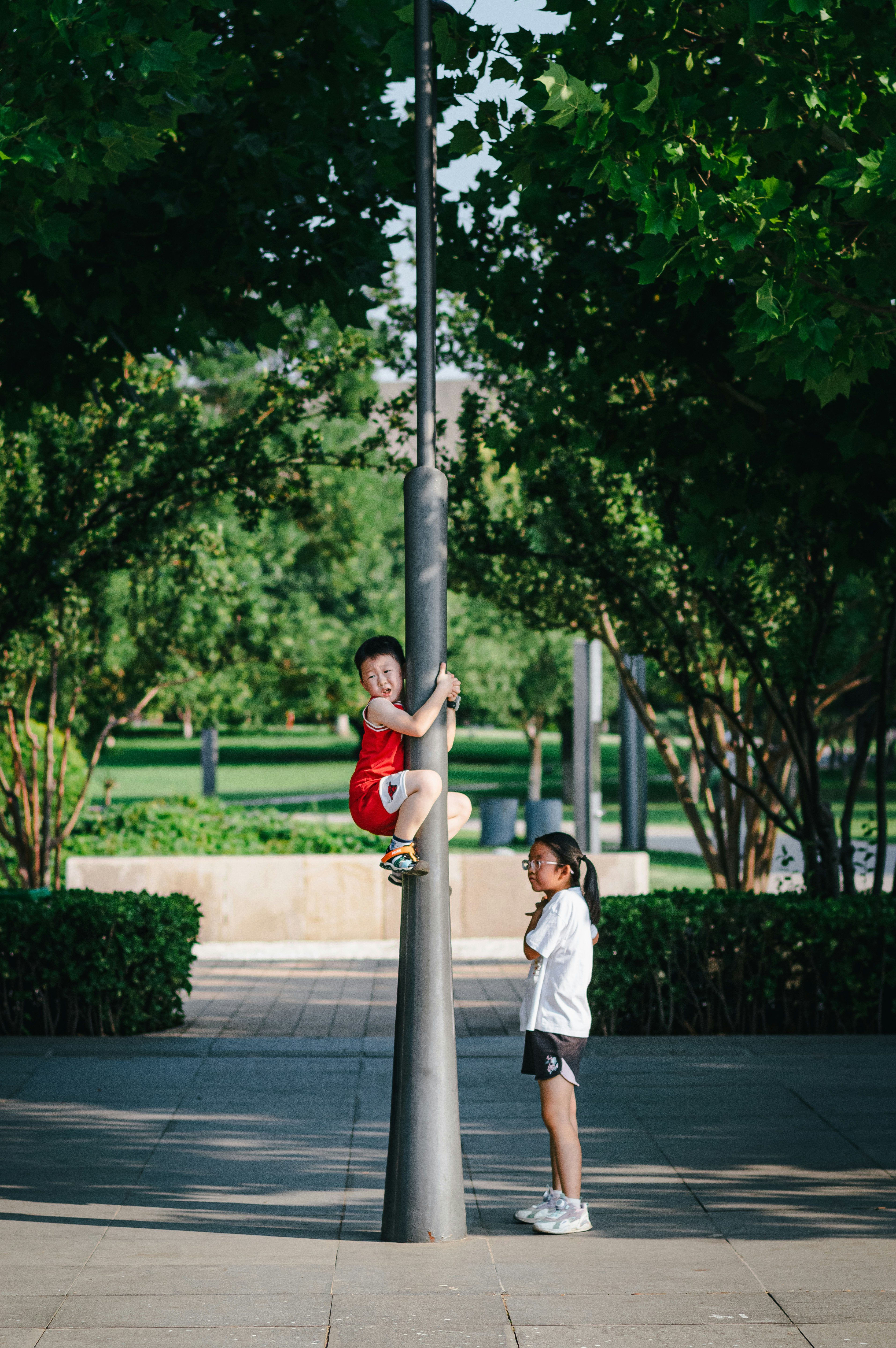 A boy climbs a pole while a girl watches.