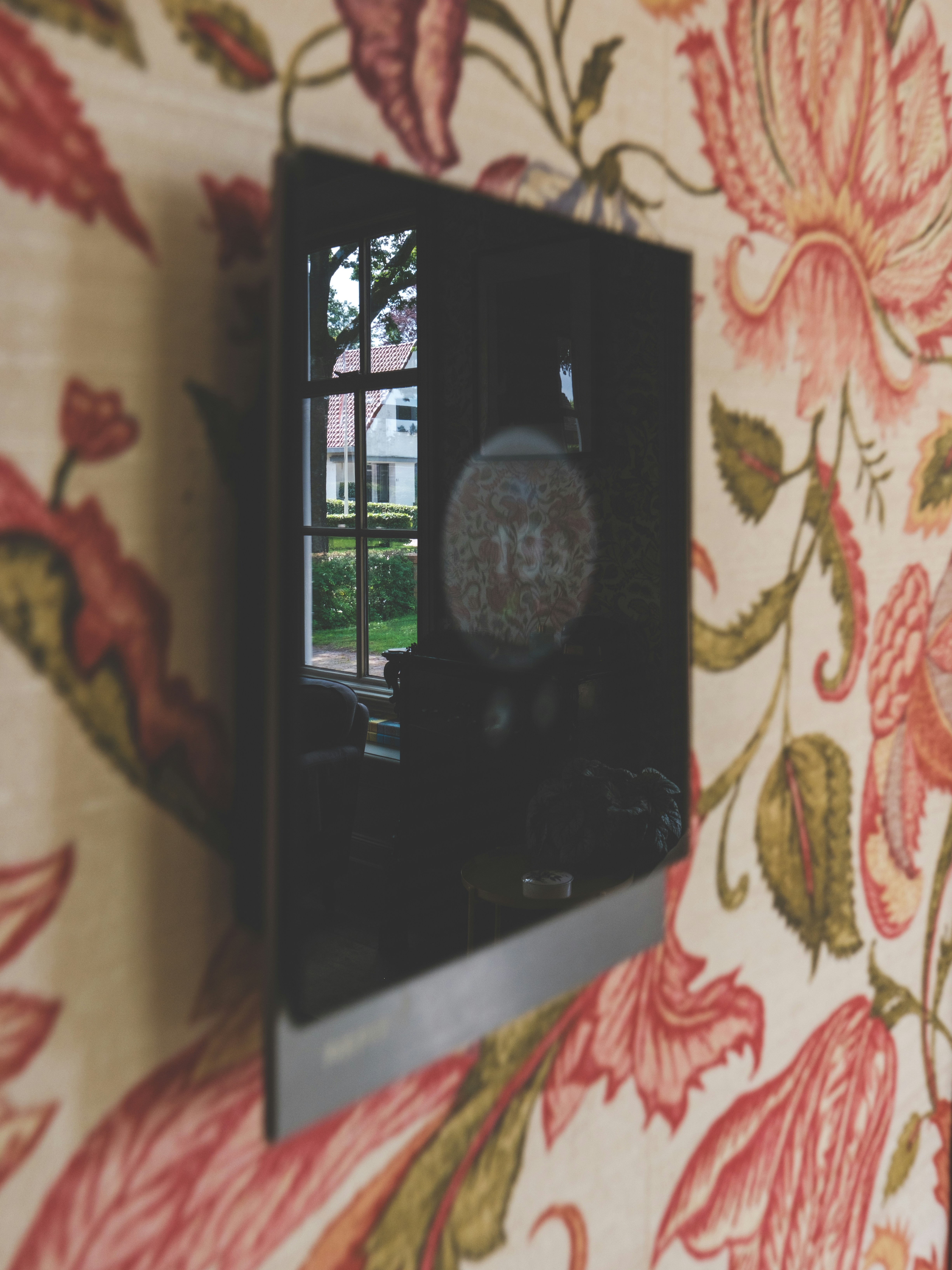 A black, digital thermostat is on a floral wallpapered wall.