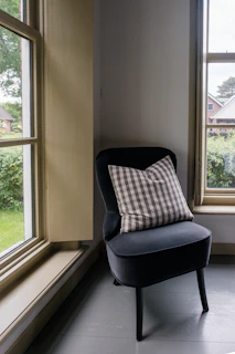 A dark chair sits next to two windows.