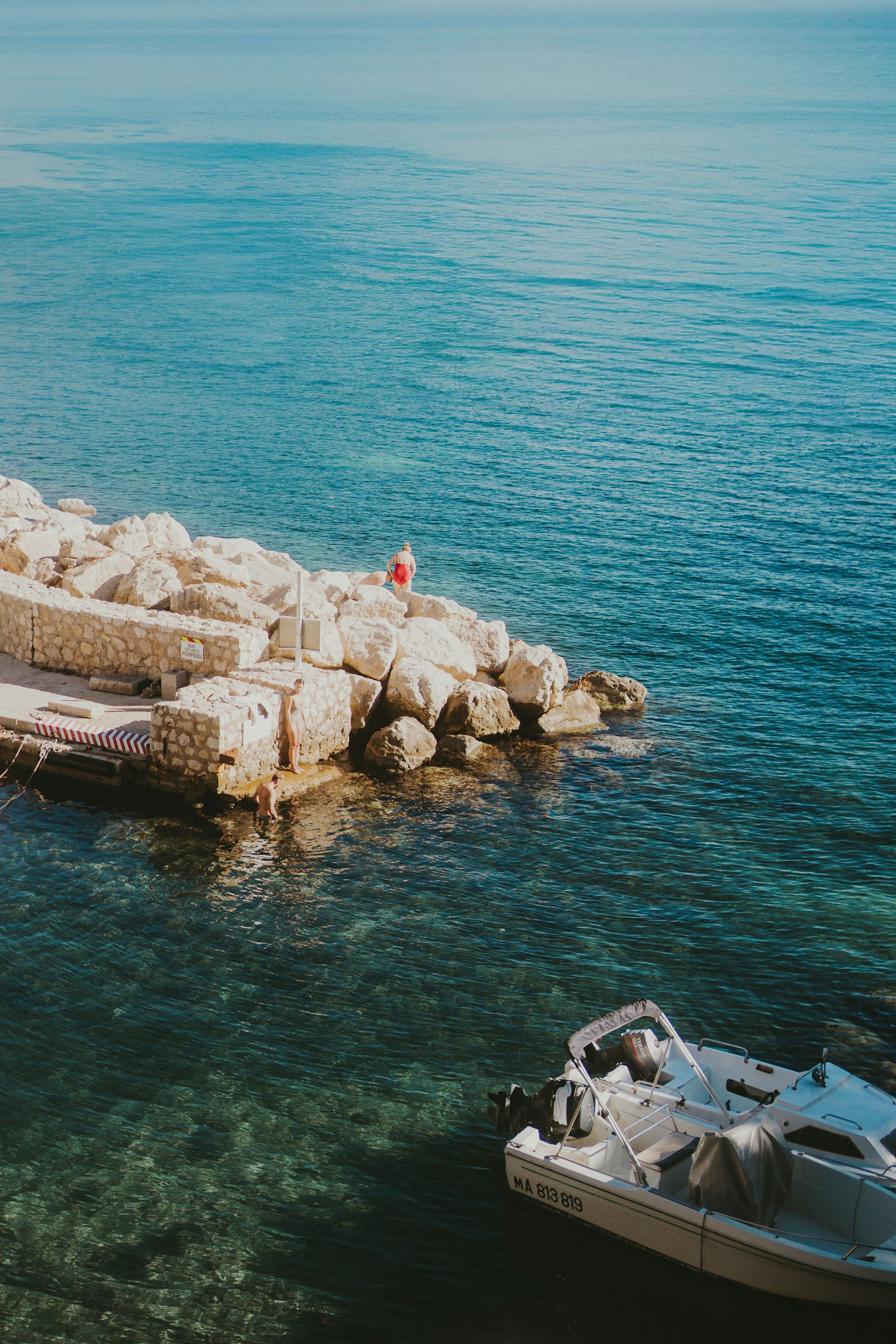 Calm, blue sea with a boat and rocky shore.