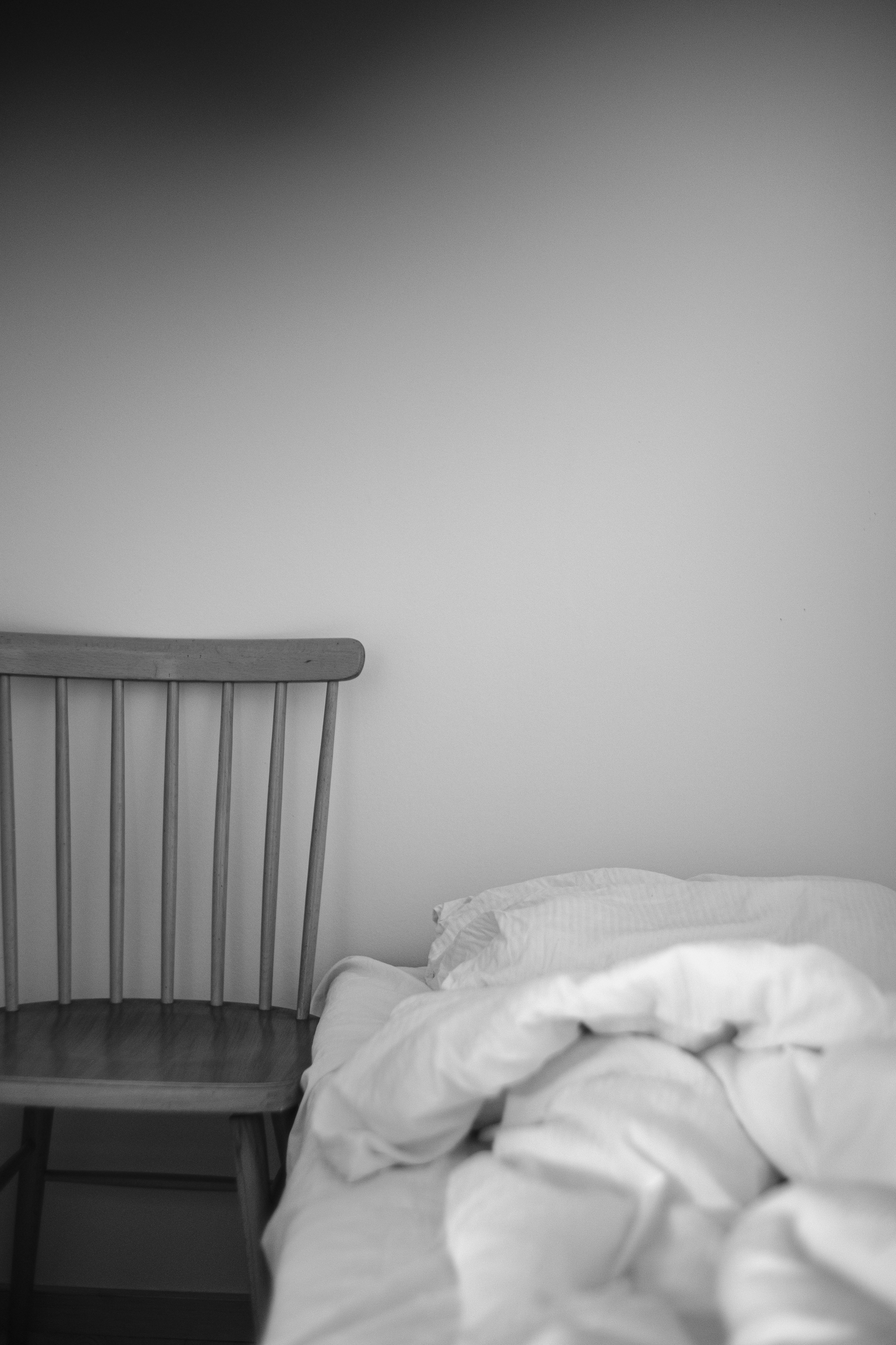 An undone bed next to a simple chair.