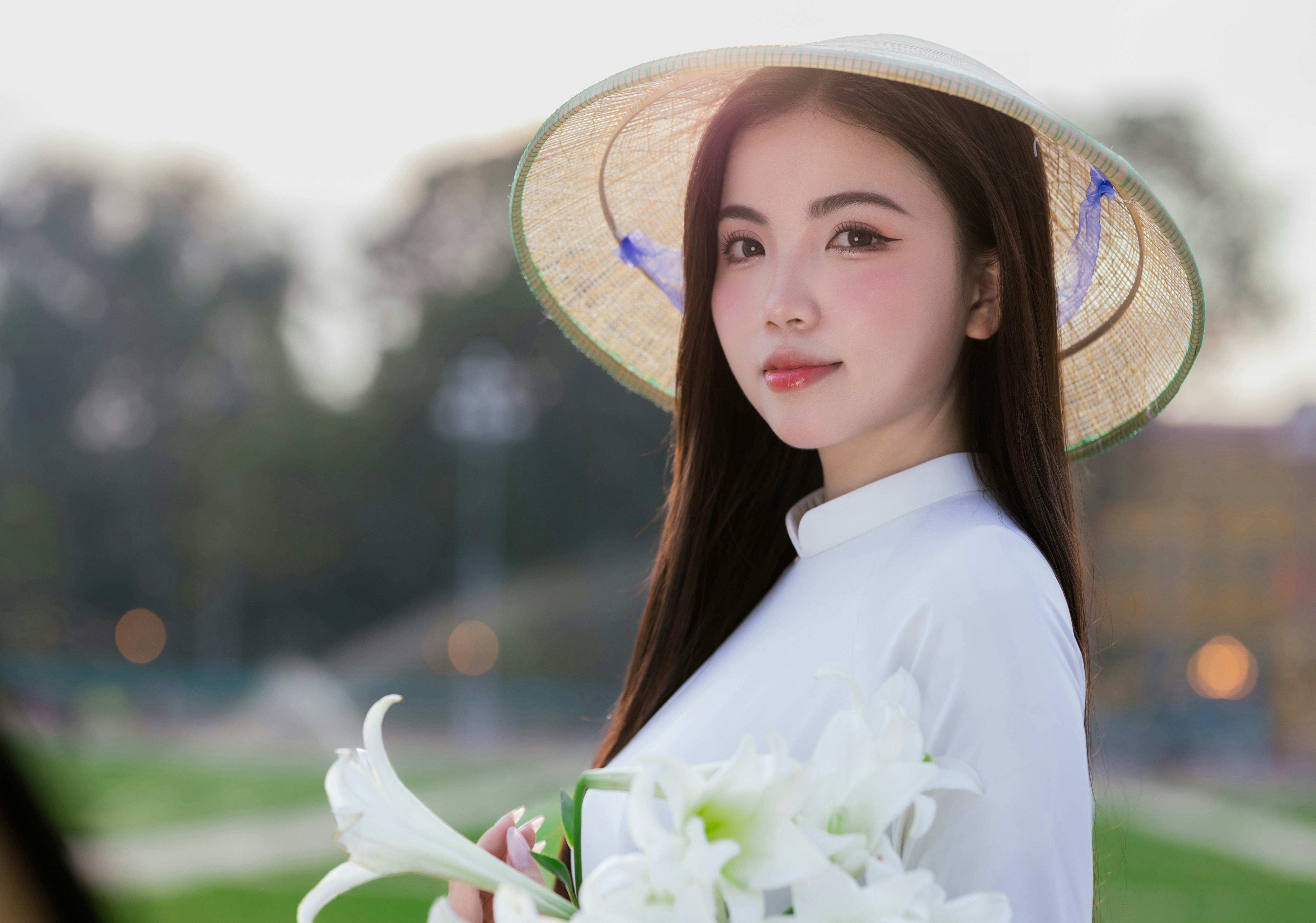 Woman wears hat and holds flowers, looking at the camera.