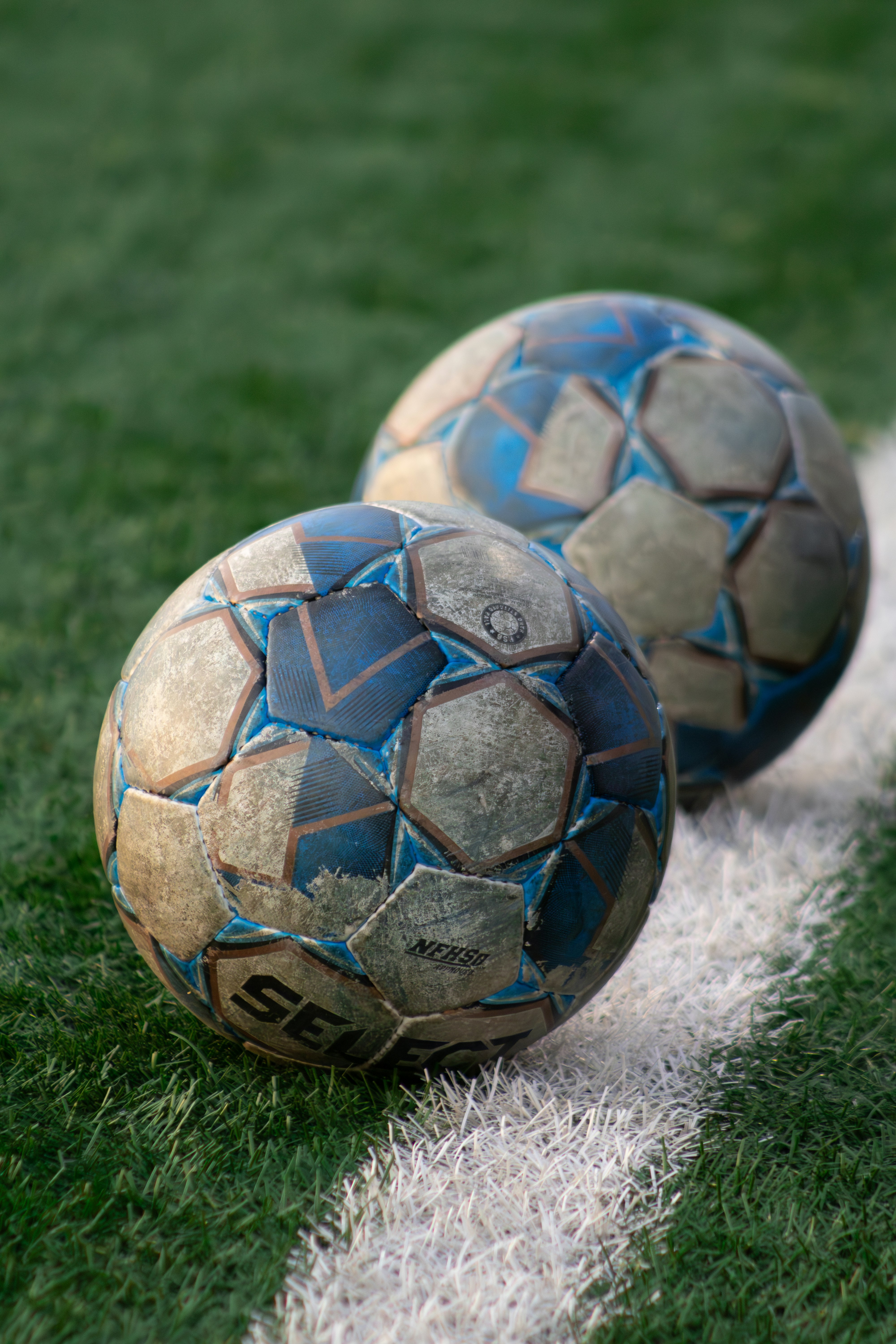 Two soccer balls sit on a white sideline.